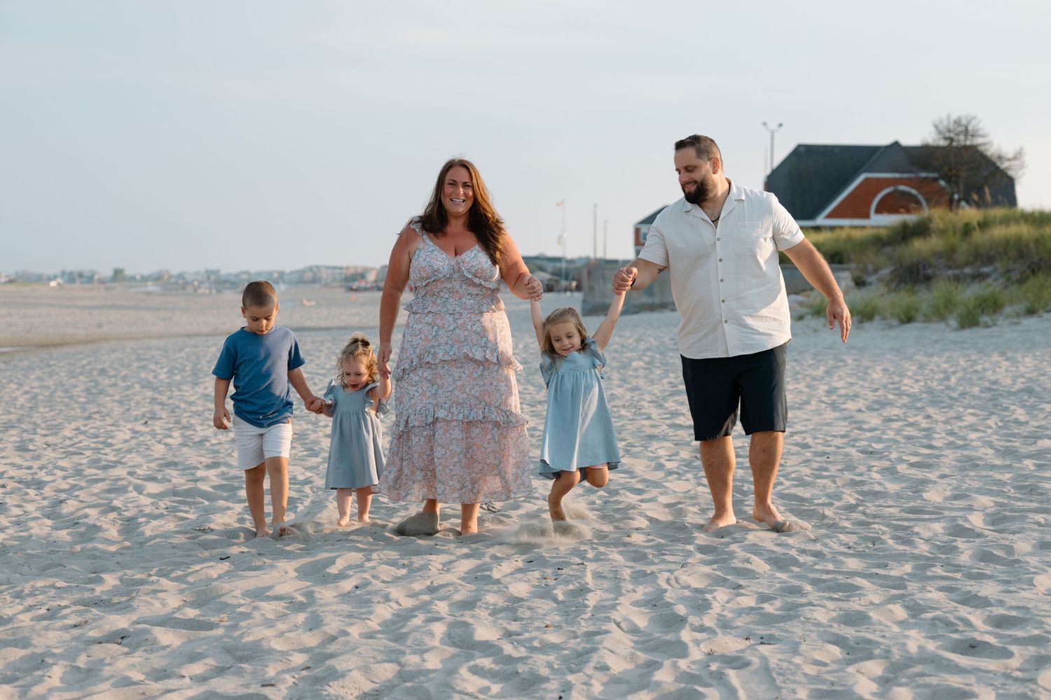 Family walking together hand in hand on sandy beach at sunset.