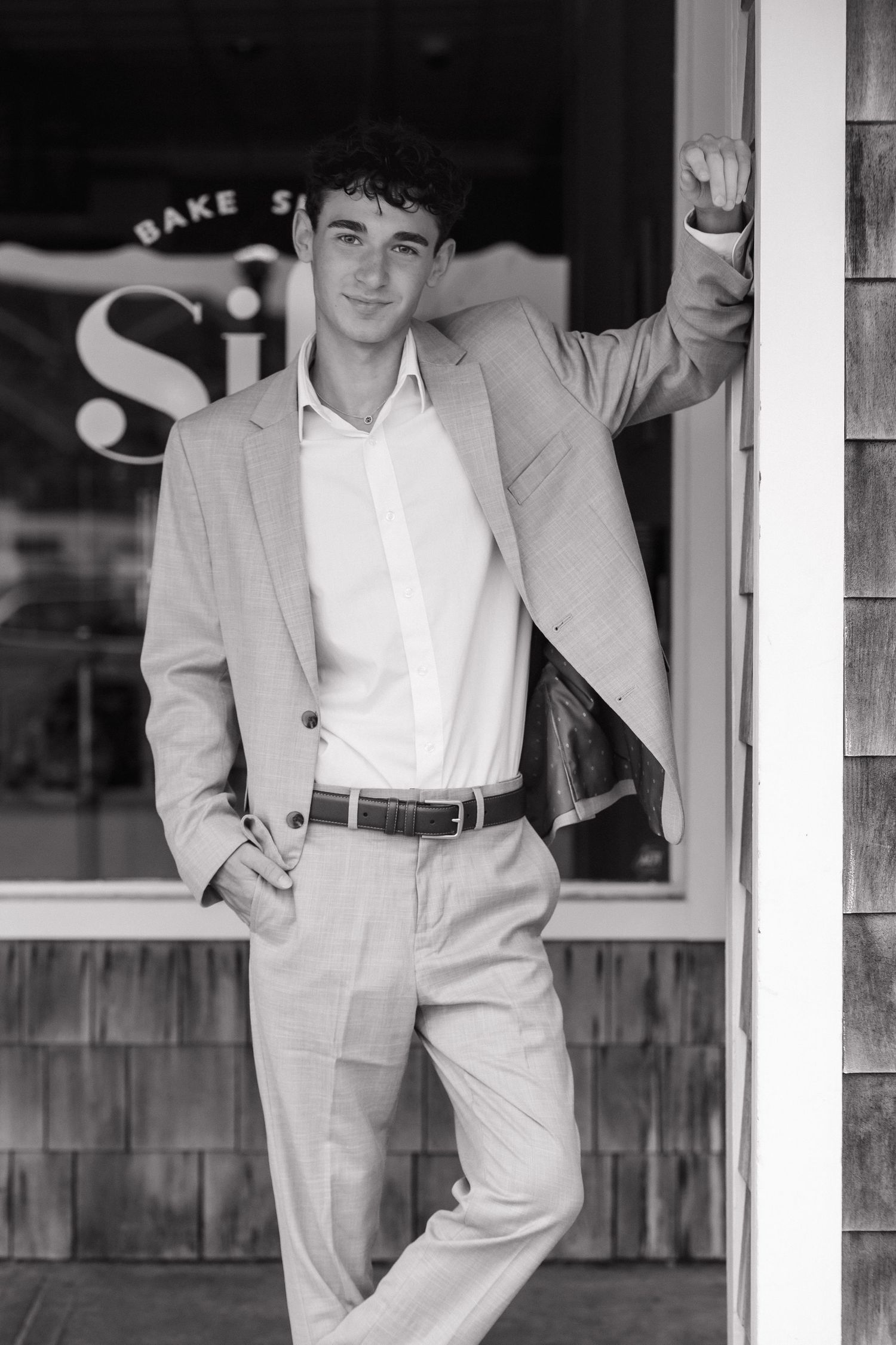 Black and white photo showing someone in a light-colored suit leaning against a storefront exterior.
