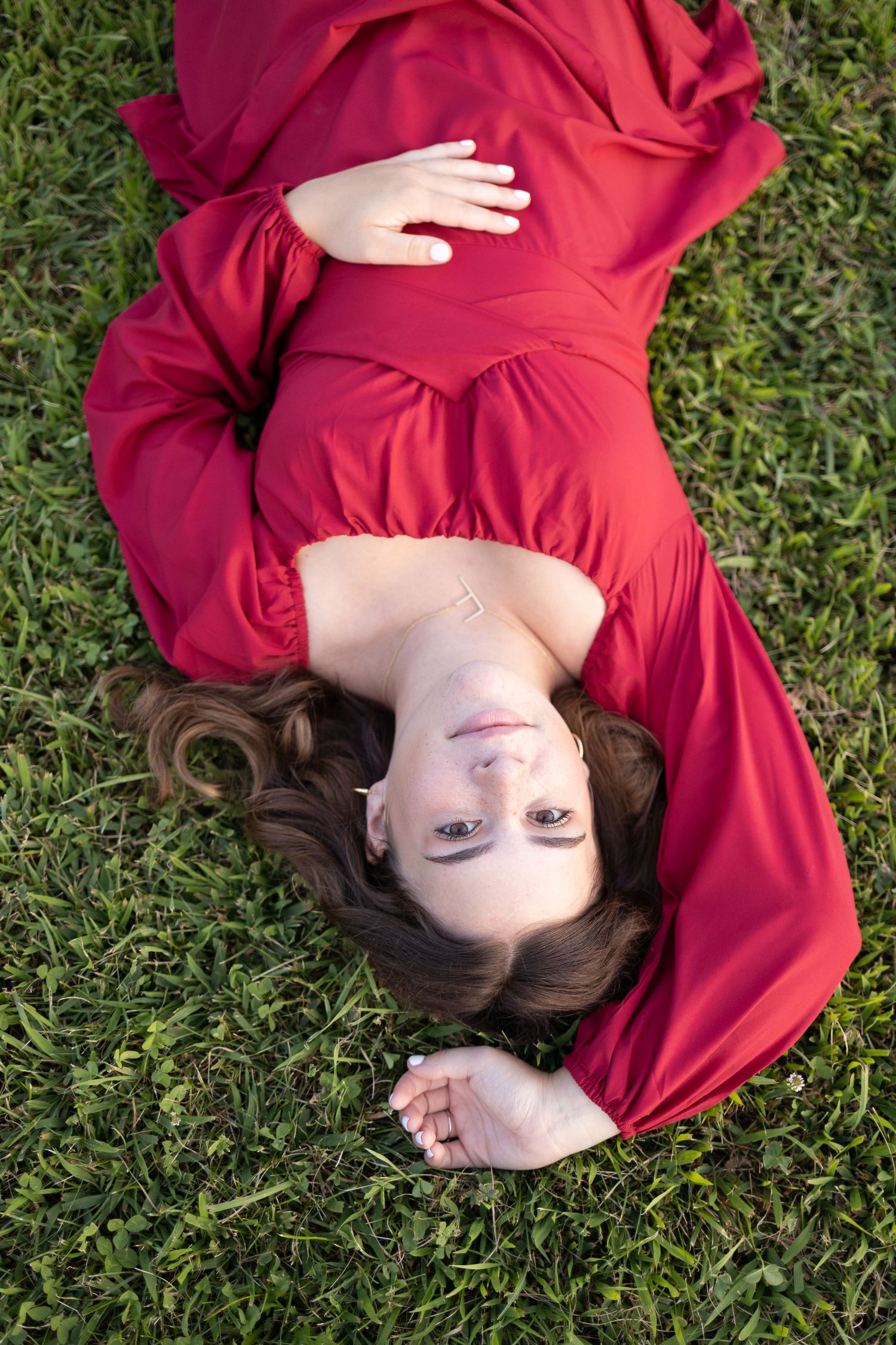 A person in a flowing red dress lies on green grass, viewed from above.