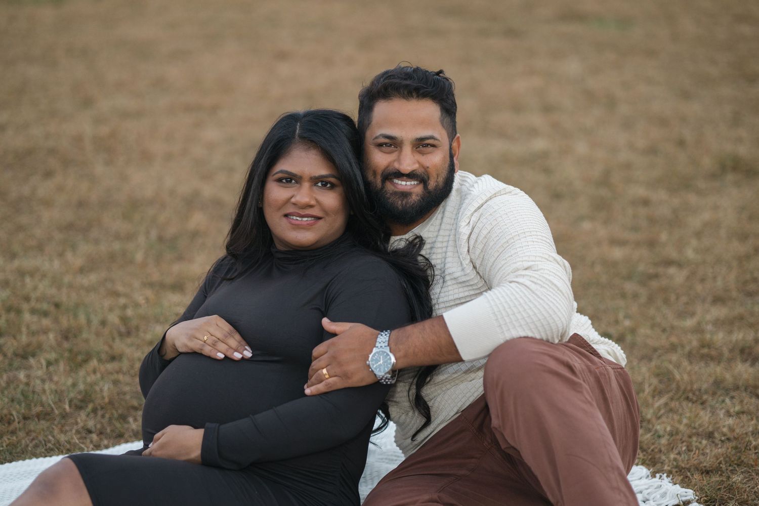 Happy couple embracing on grassy field during outdoor photoshoot.