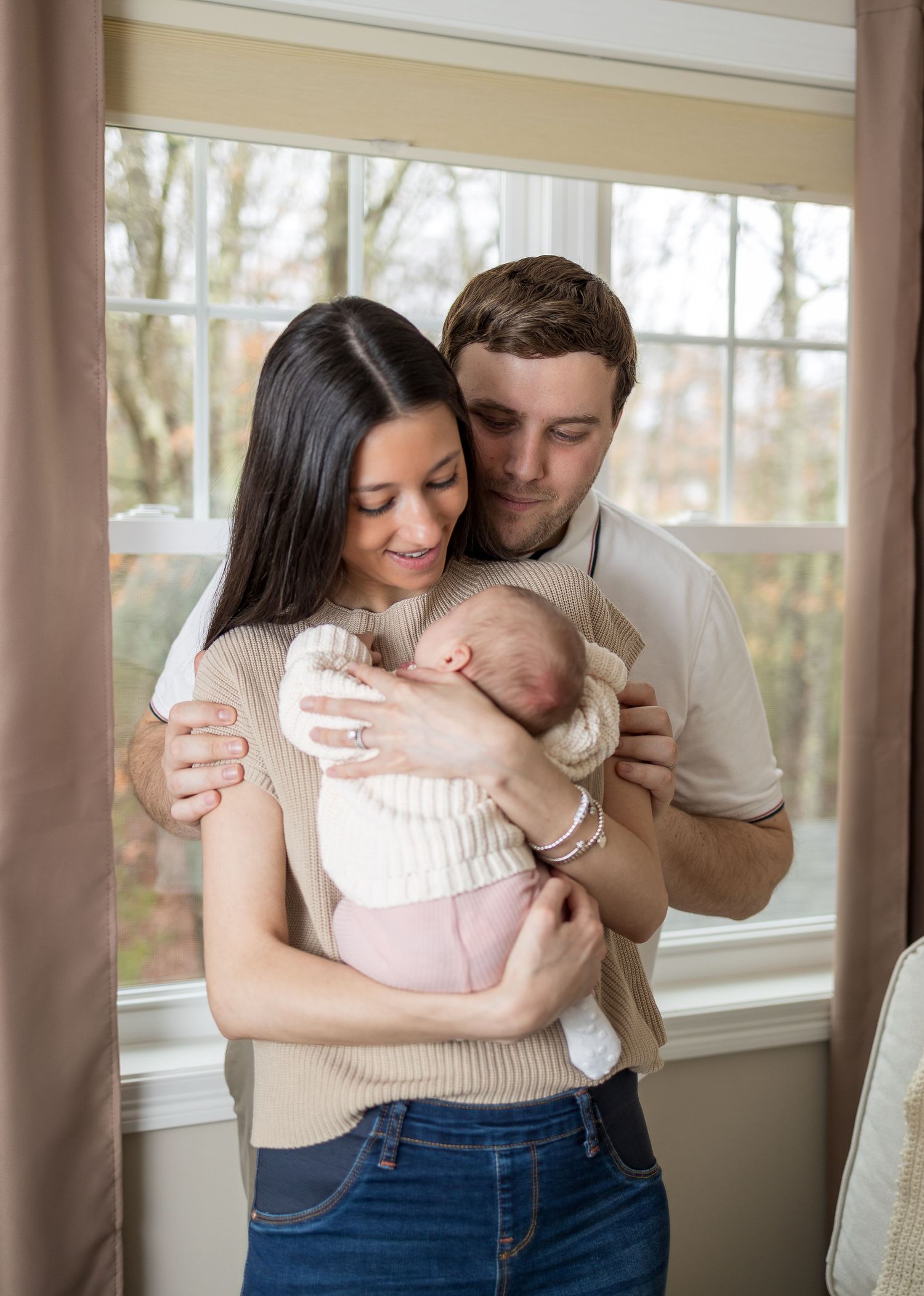 Family standing by window sharing intimate moment with newborn baby.