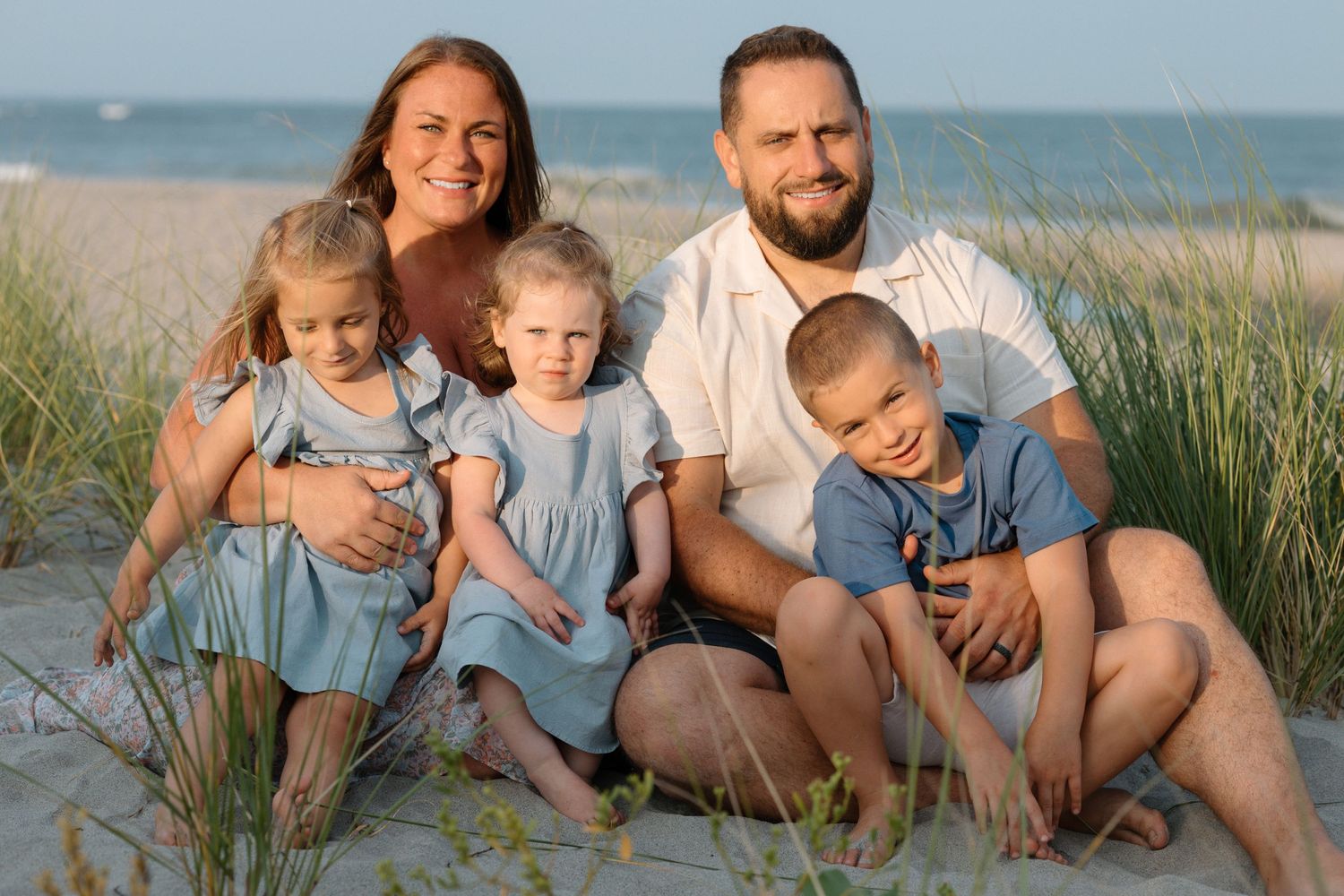 Family sitting together on sandy beach dunes during golden hour.