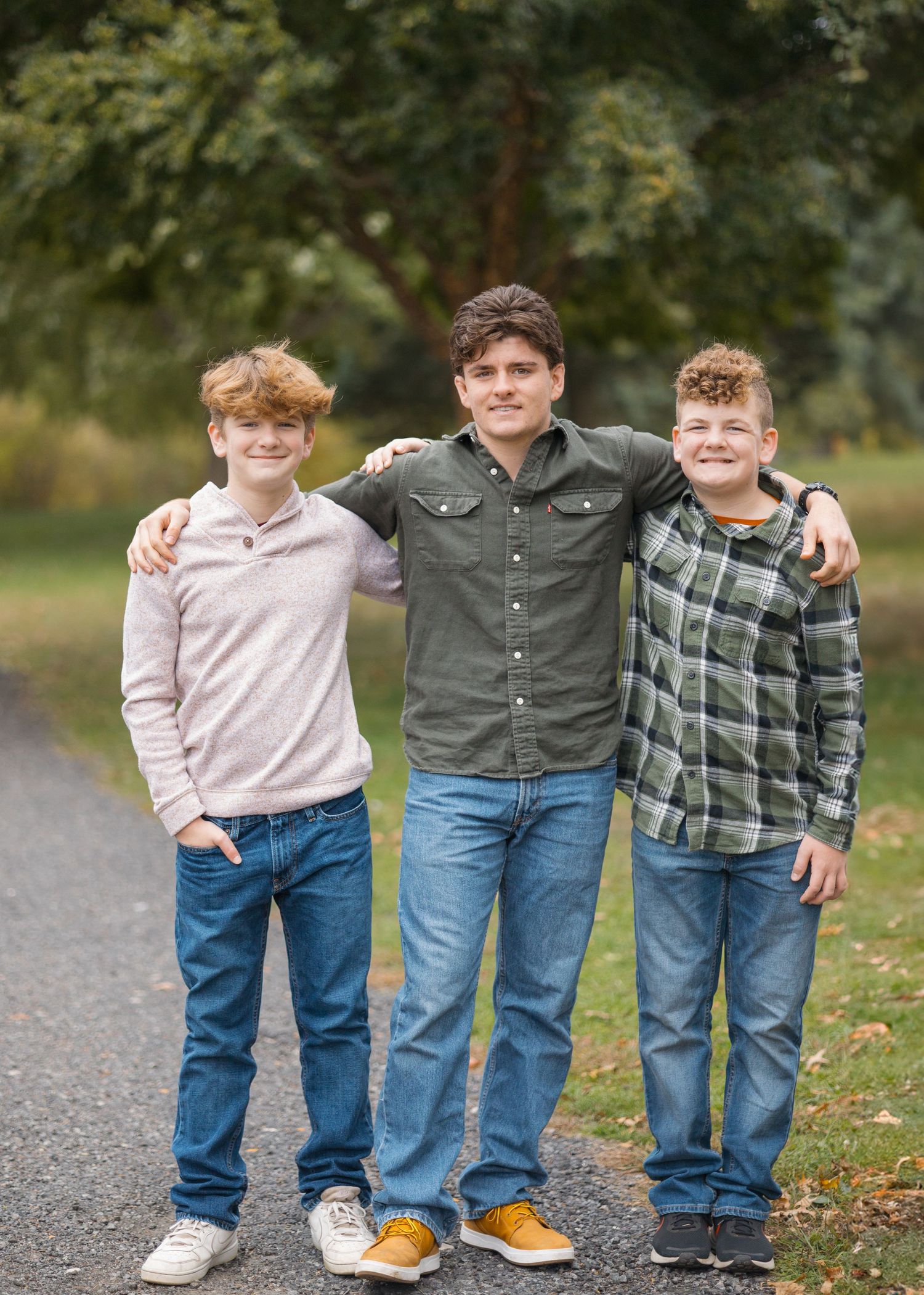 Three people pose together on a path with greenery in the background.