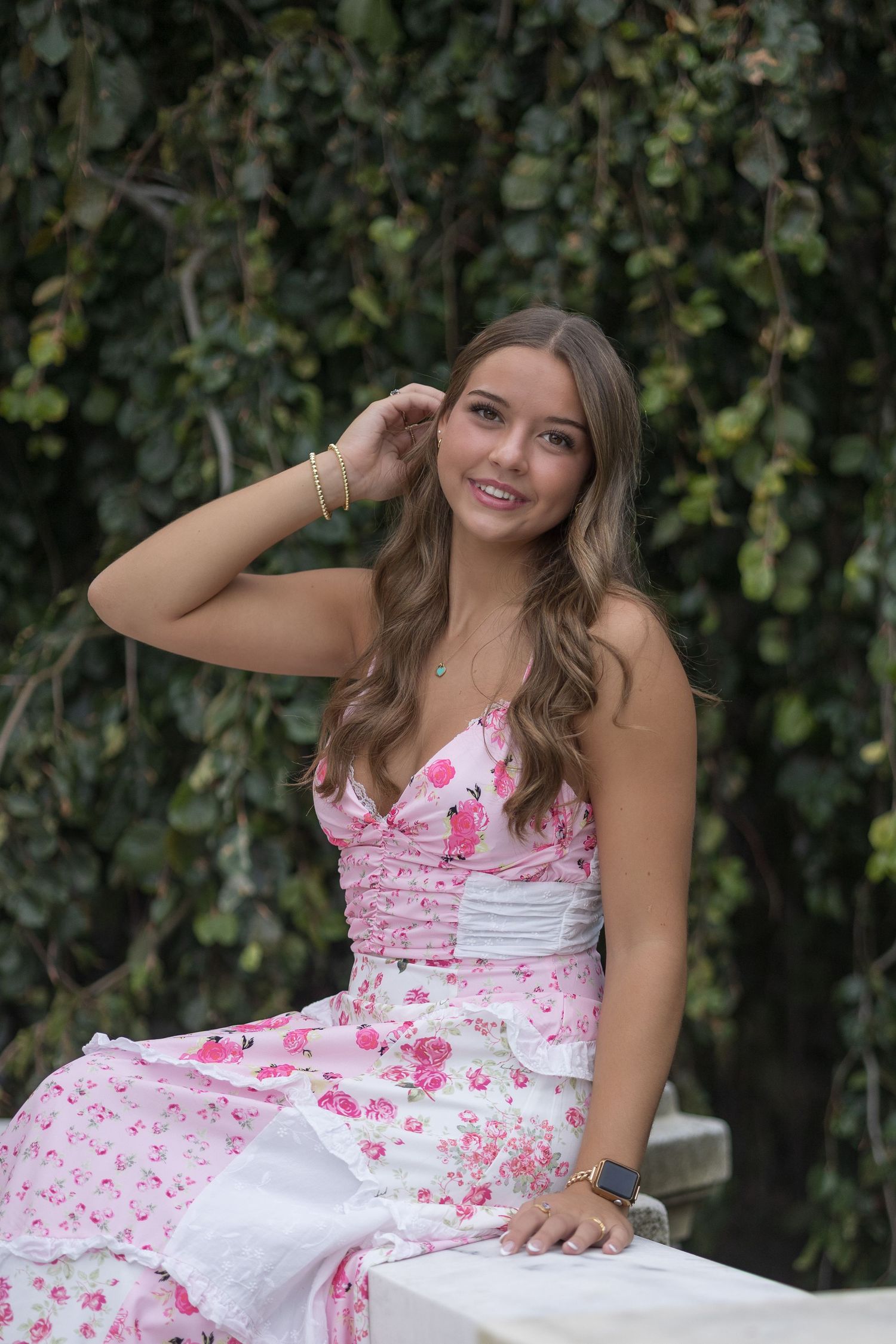 A series of outdoor portrait photos featuring a floral pink and white summer dress against a leafy background.