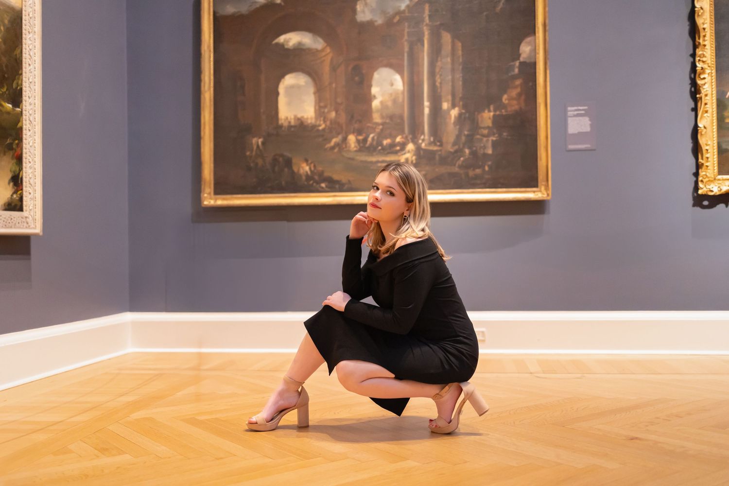 Artistic portrait in a museum gallery with classical paintings and wooden flooring.