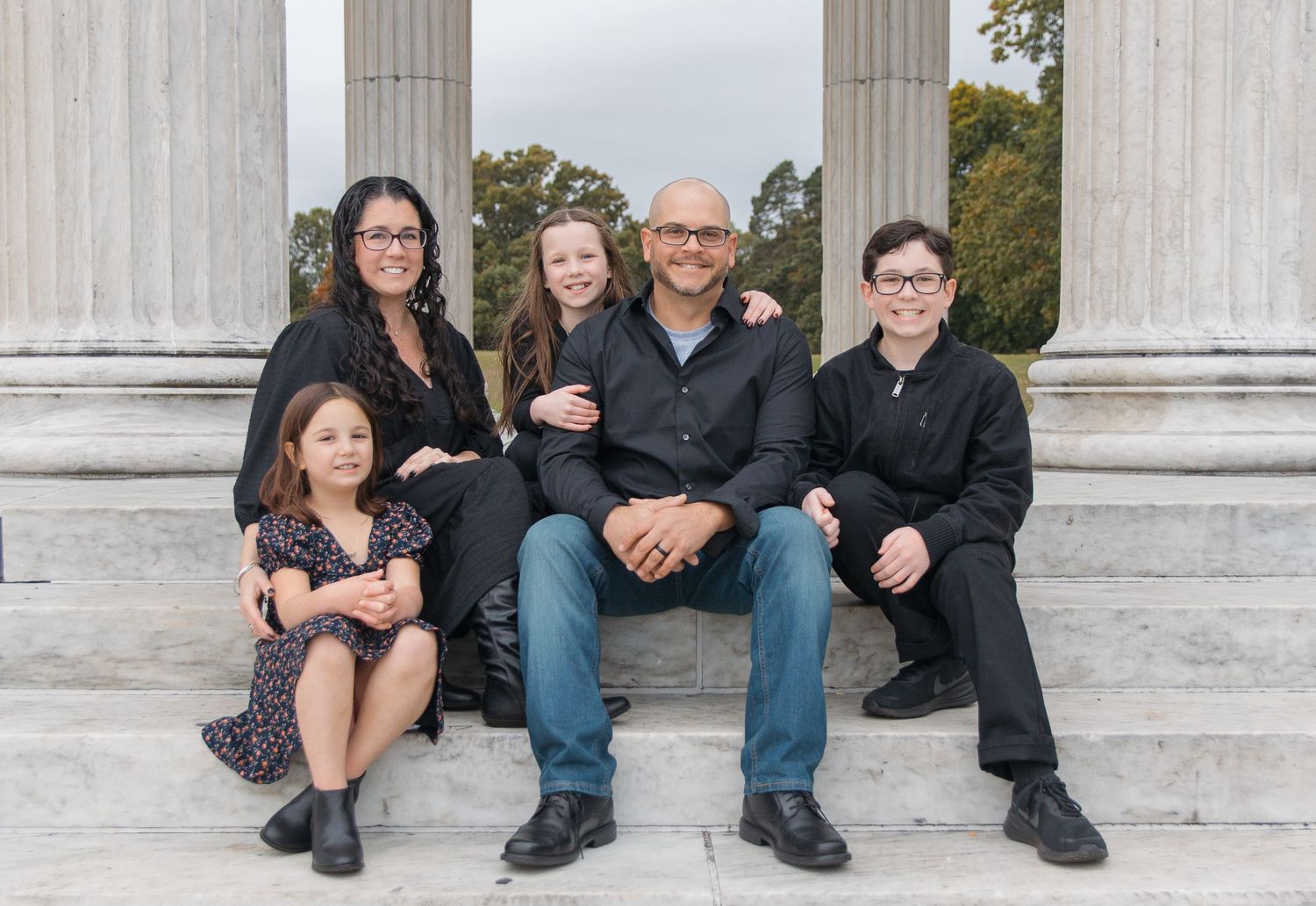 A family sits on stone steps with classic white columns behind them.