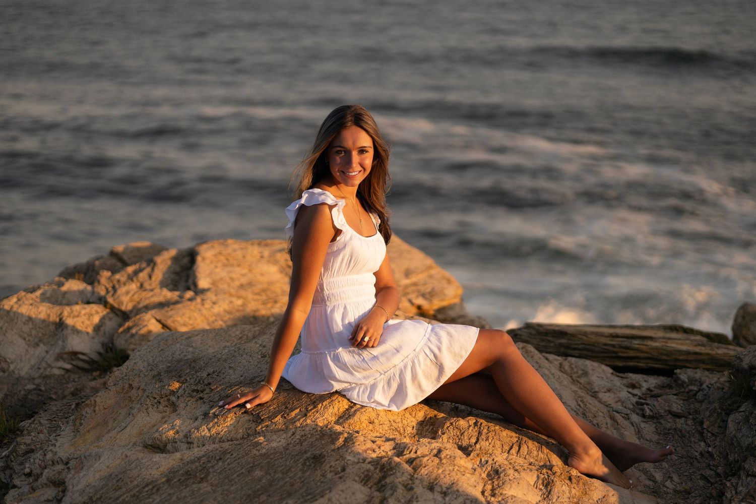 A white dress contrasts against coastal rocks during sunset by the ocean.