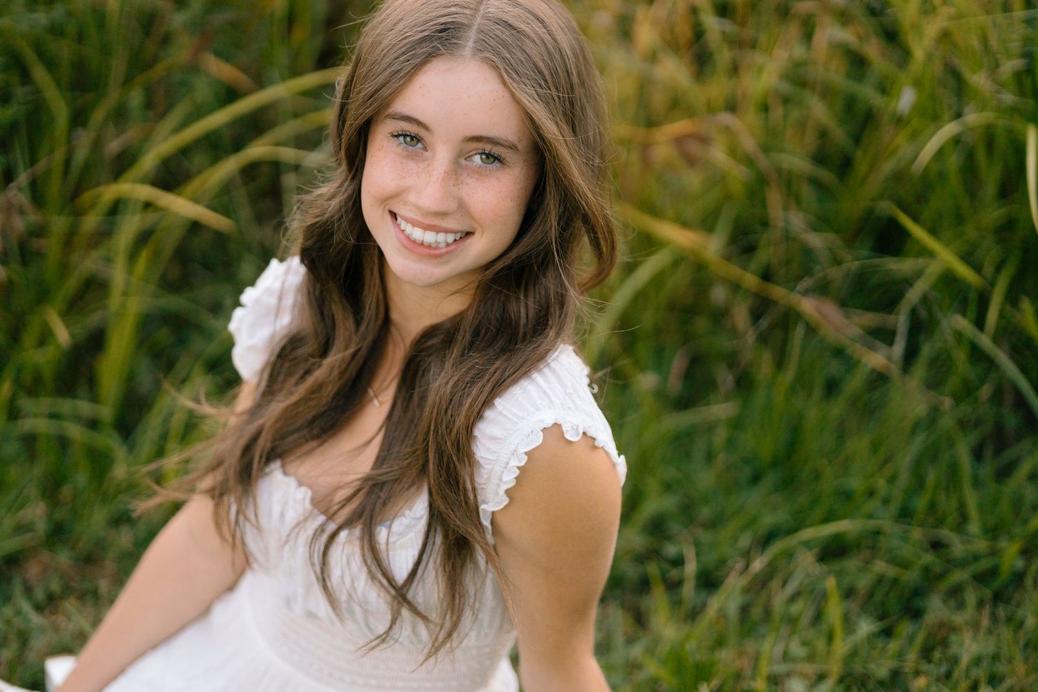 A person in a white lace dress poses against a natural backdrop of tall grass.