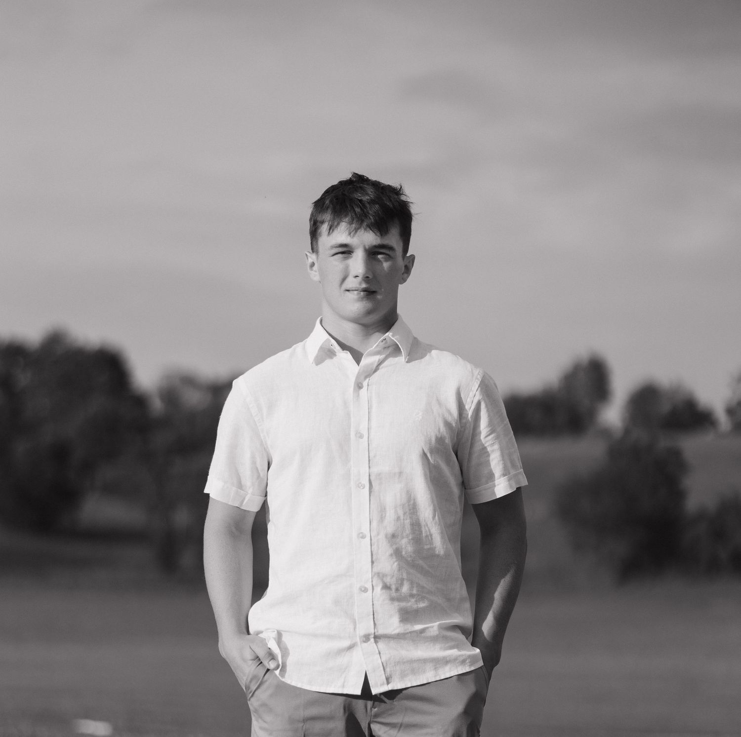 A black and white portrait of someone in a white button-down shirt against a blurred background.