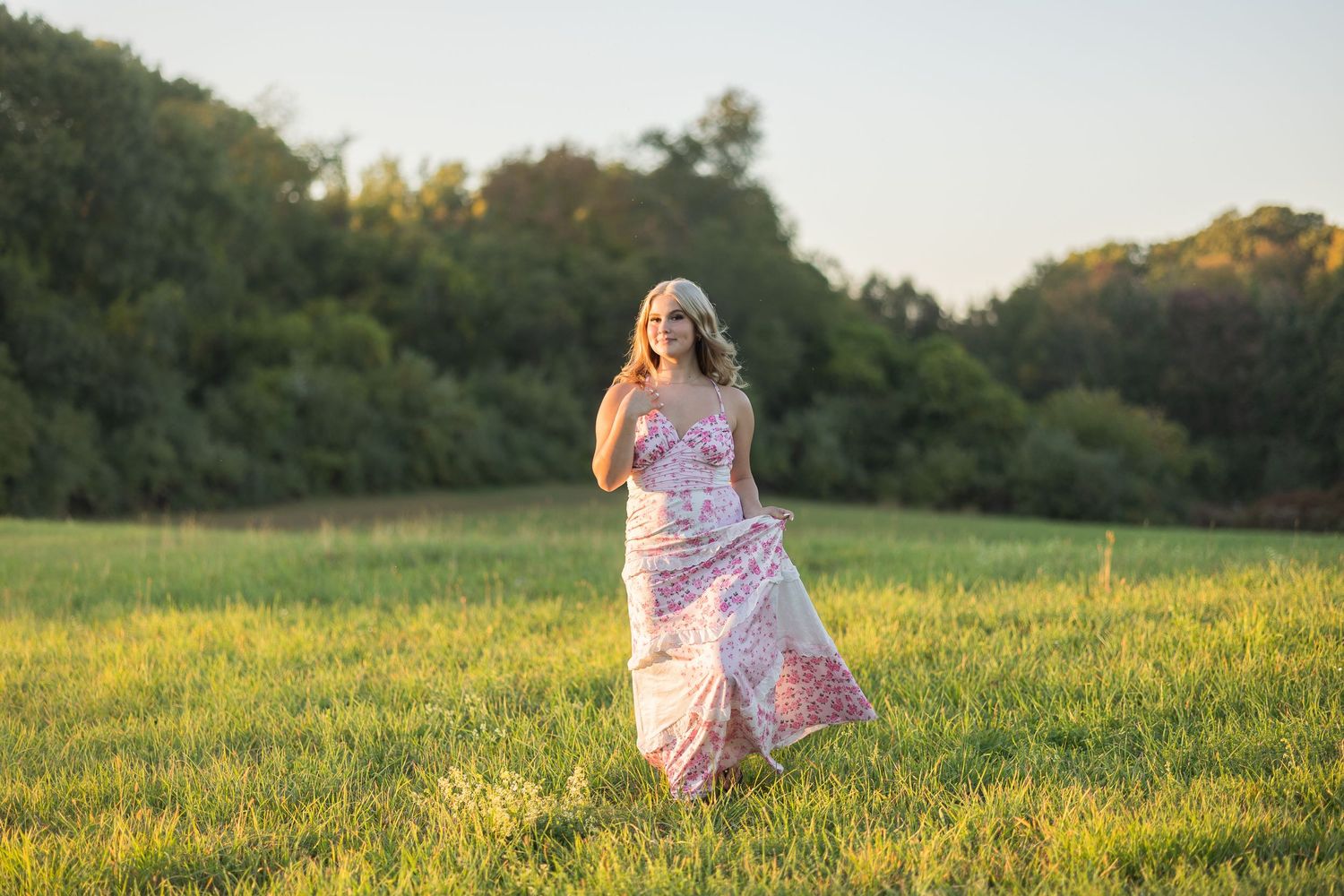A figure in a flowing pink dress twirls through a sunlit meadow during golden hour.