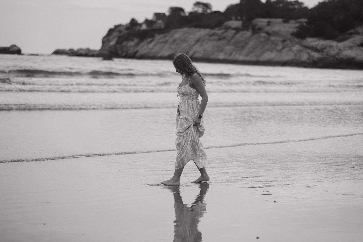 Black and white beach scene showing footprints in the sand along a scenic coastline with cliffs in the background.