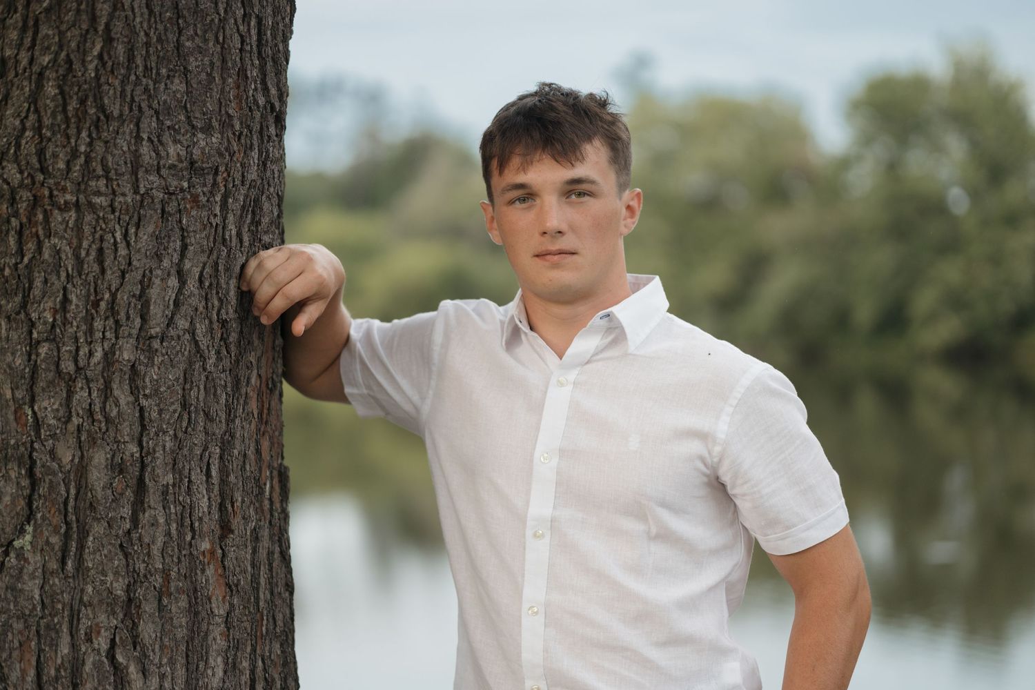 A casual outdoor portrait by a tree with a lake in the background.