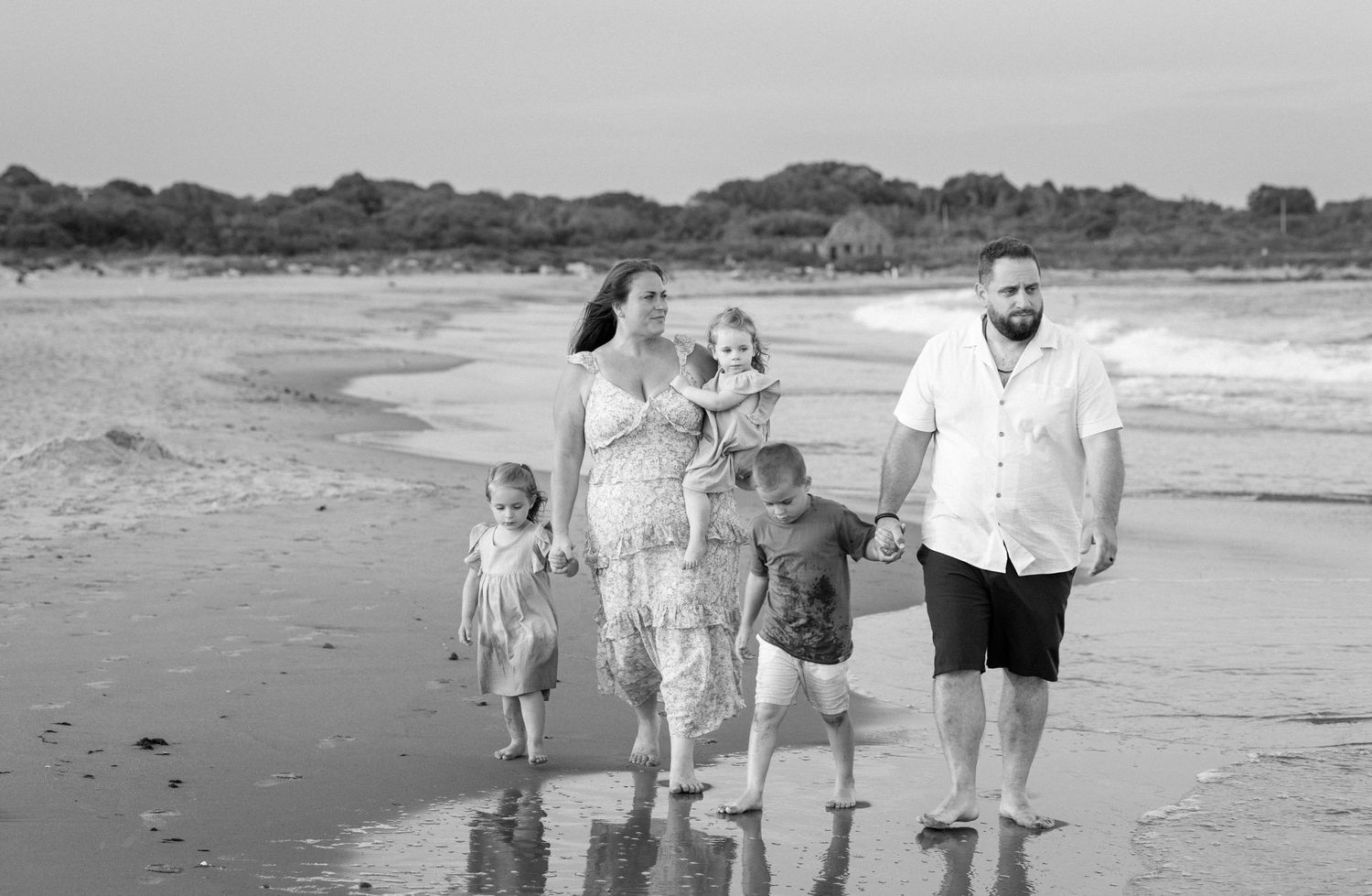 A family walking along the shoreline during a black and white beach photoshoot.