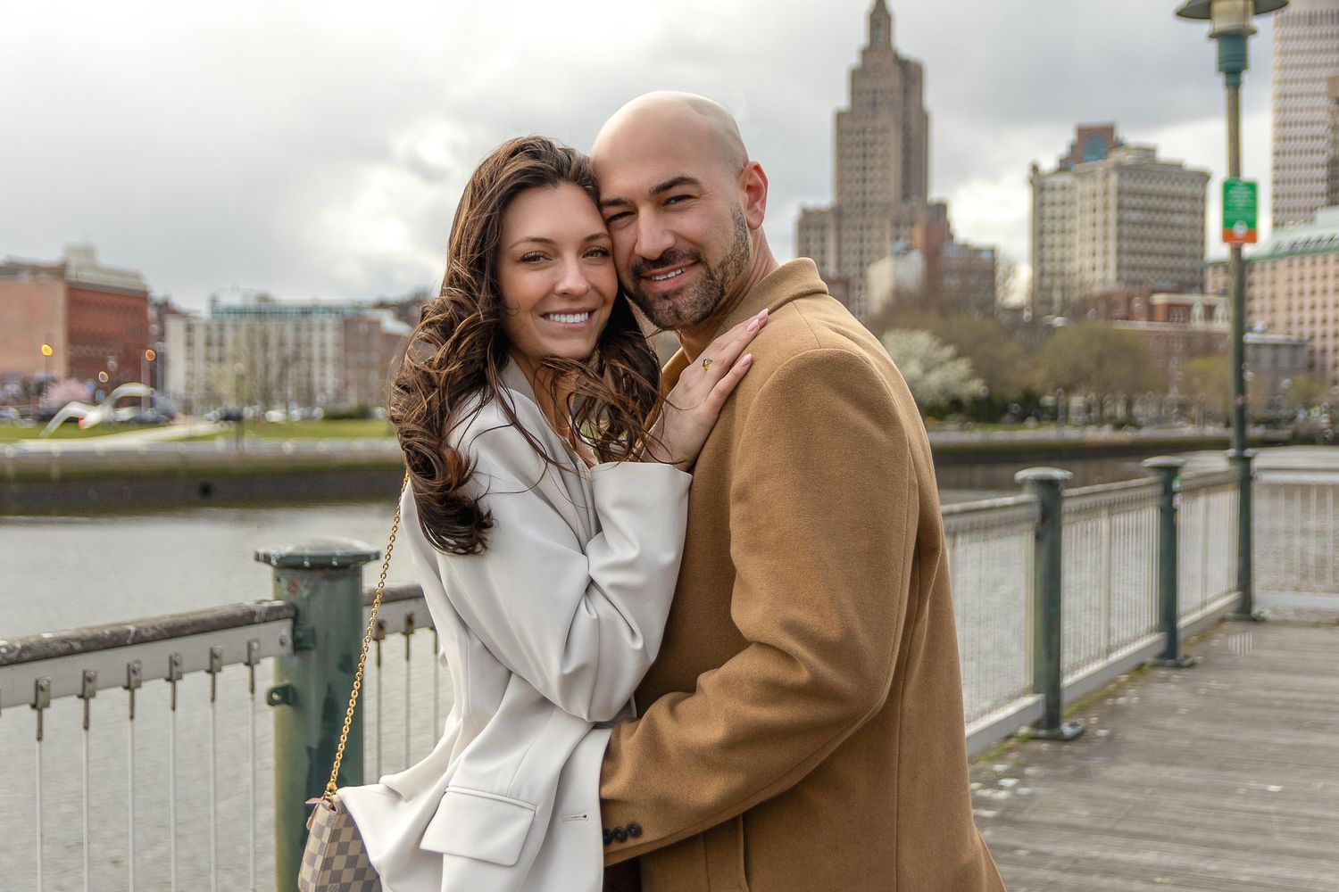 Couple embracing on waterfront with urban skyline in background.