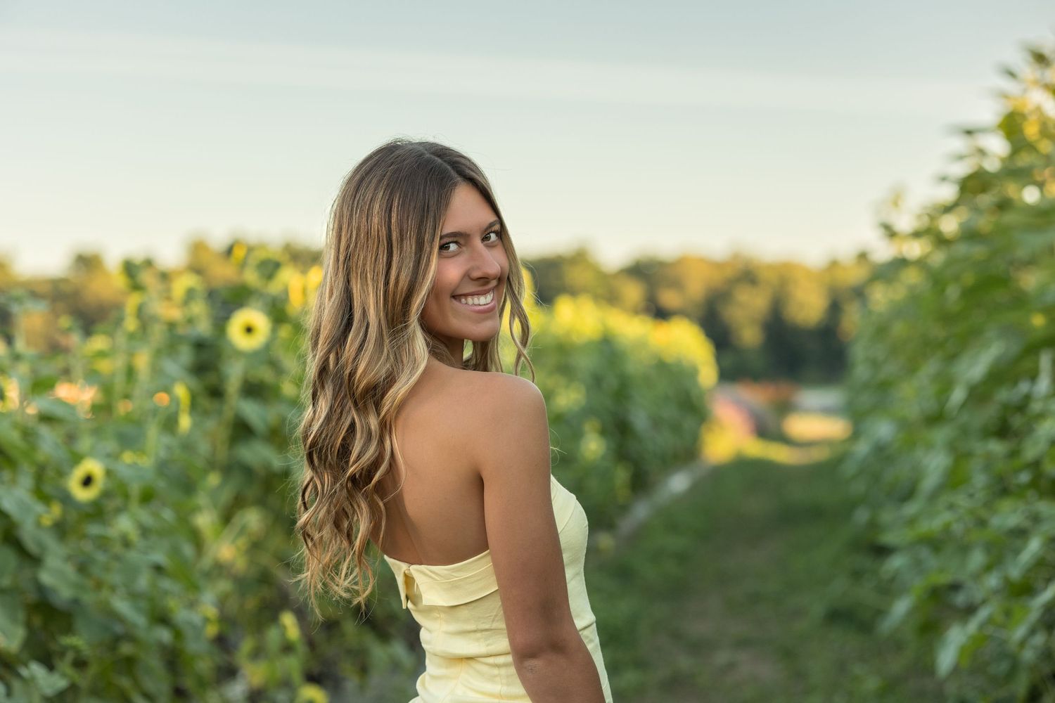 Someone in a yellow dress poses in a sunflower field during golden hour with warm summer lighting.