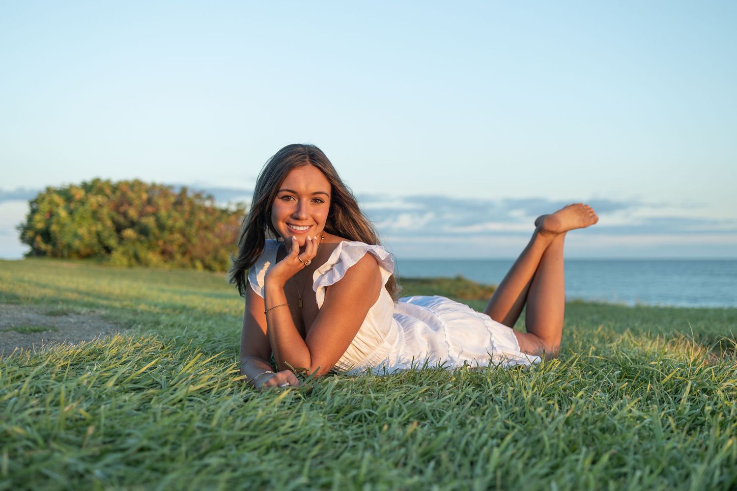 A white dress is worn while lying in green grass overlooking the ocean.