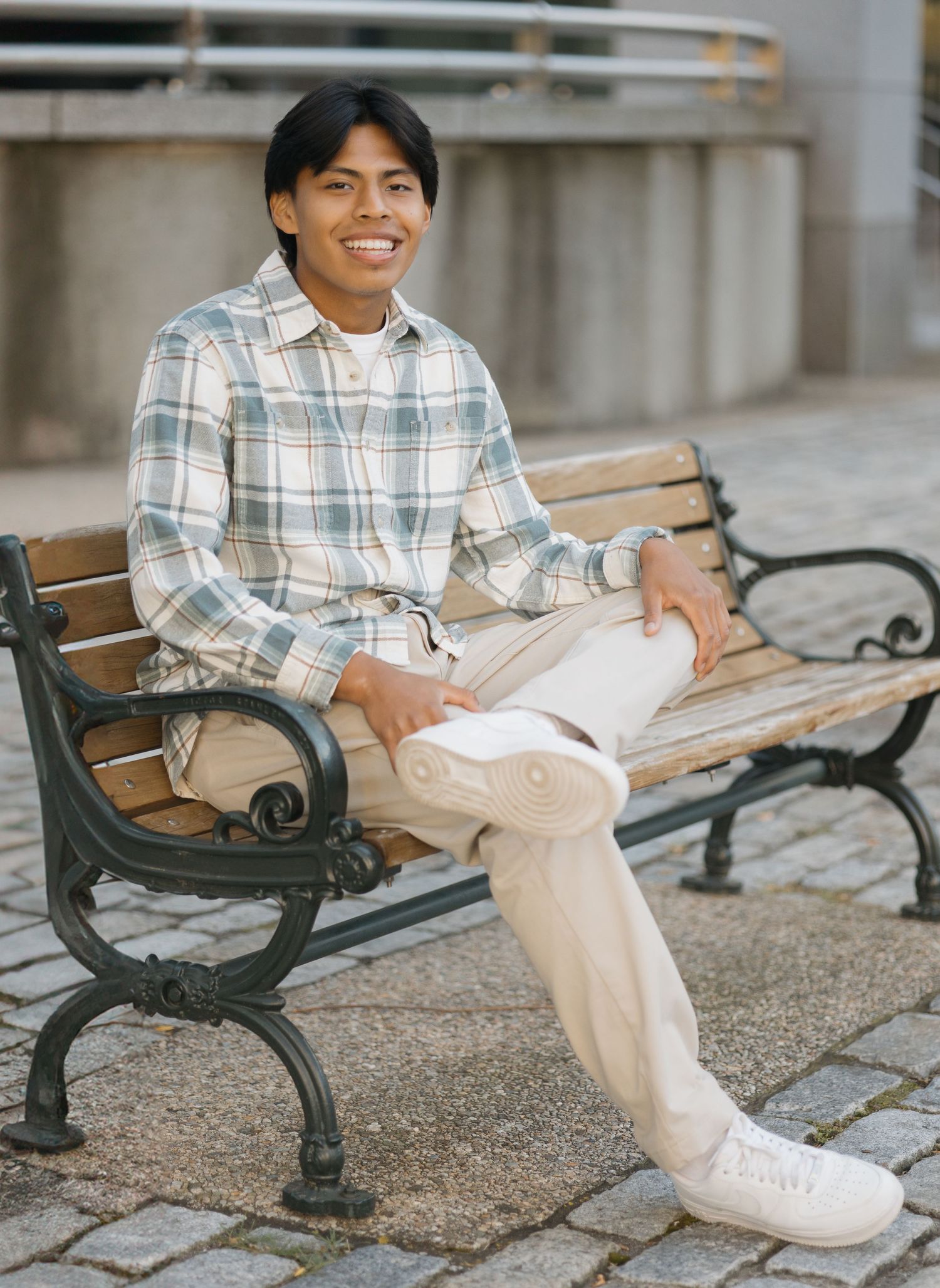 Person relaxes on ornate park bench wearing plaid shirt and khaki pants with white sneakers.