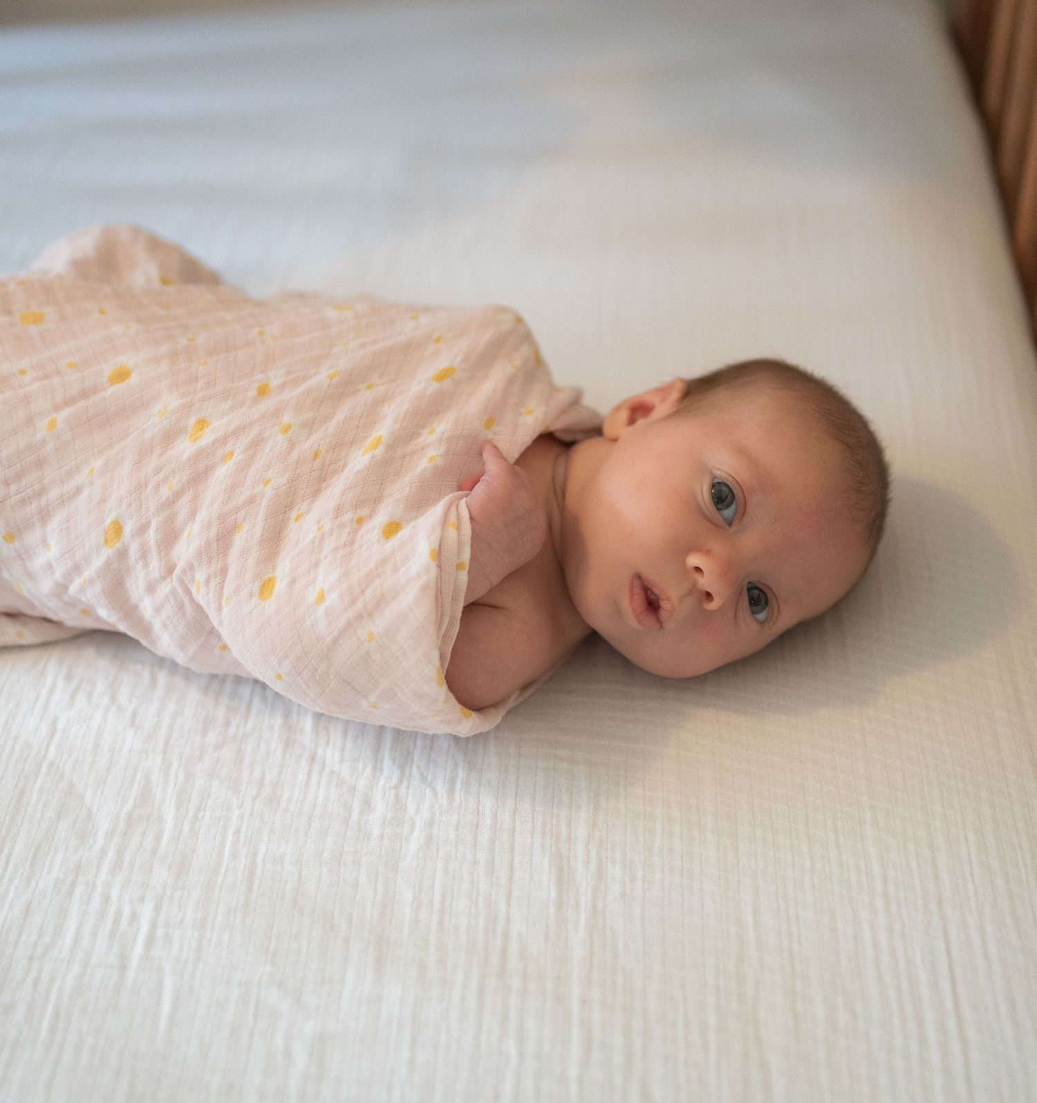 Baby in pink onesie lying on white bed sheets.