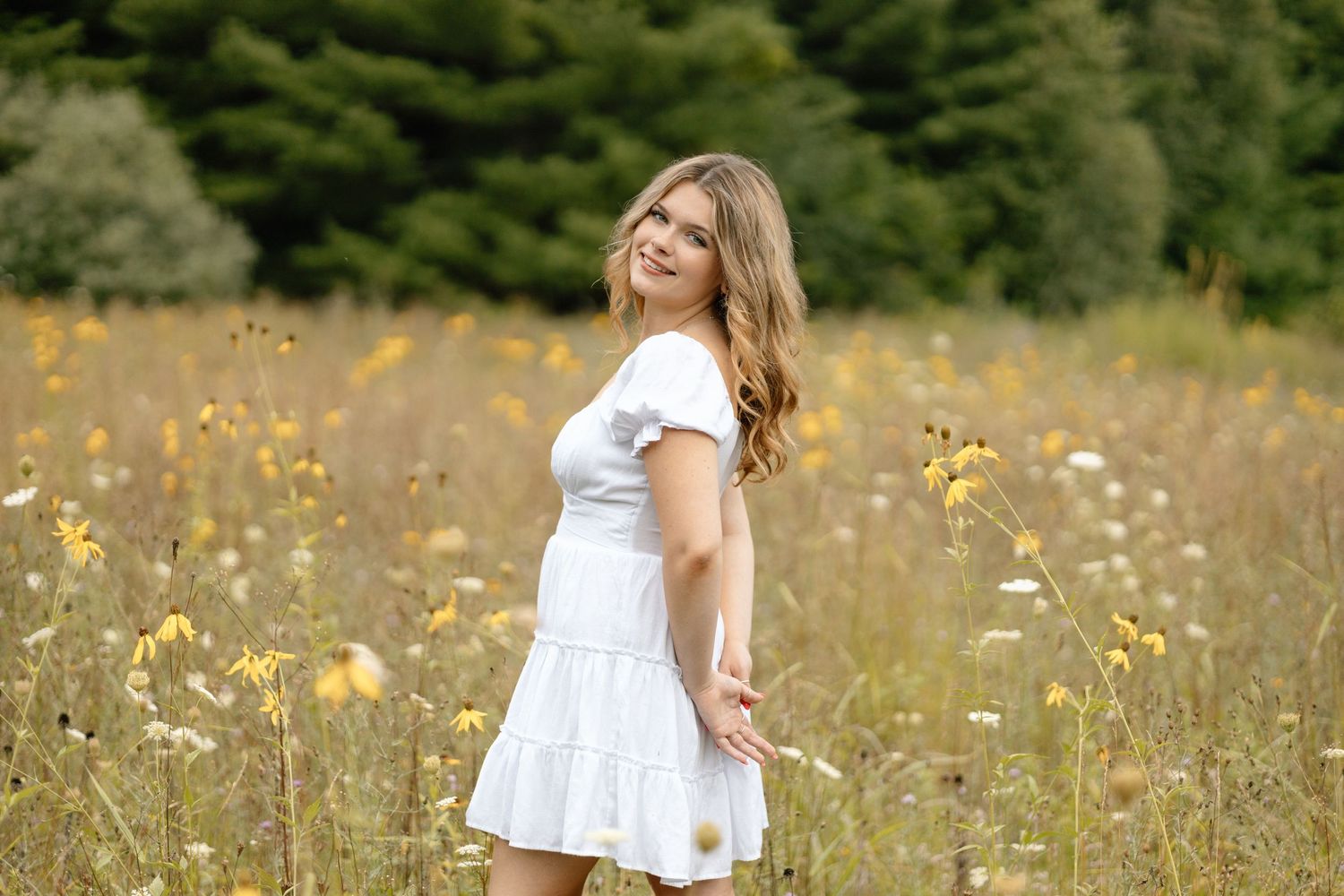 A white sundress twirls in a meadow filled with yellow wildflowers and tall grass.