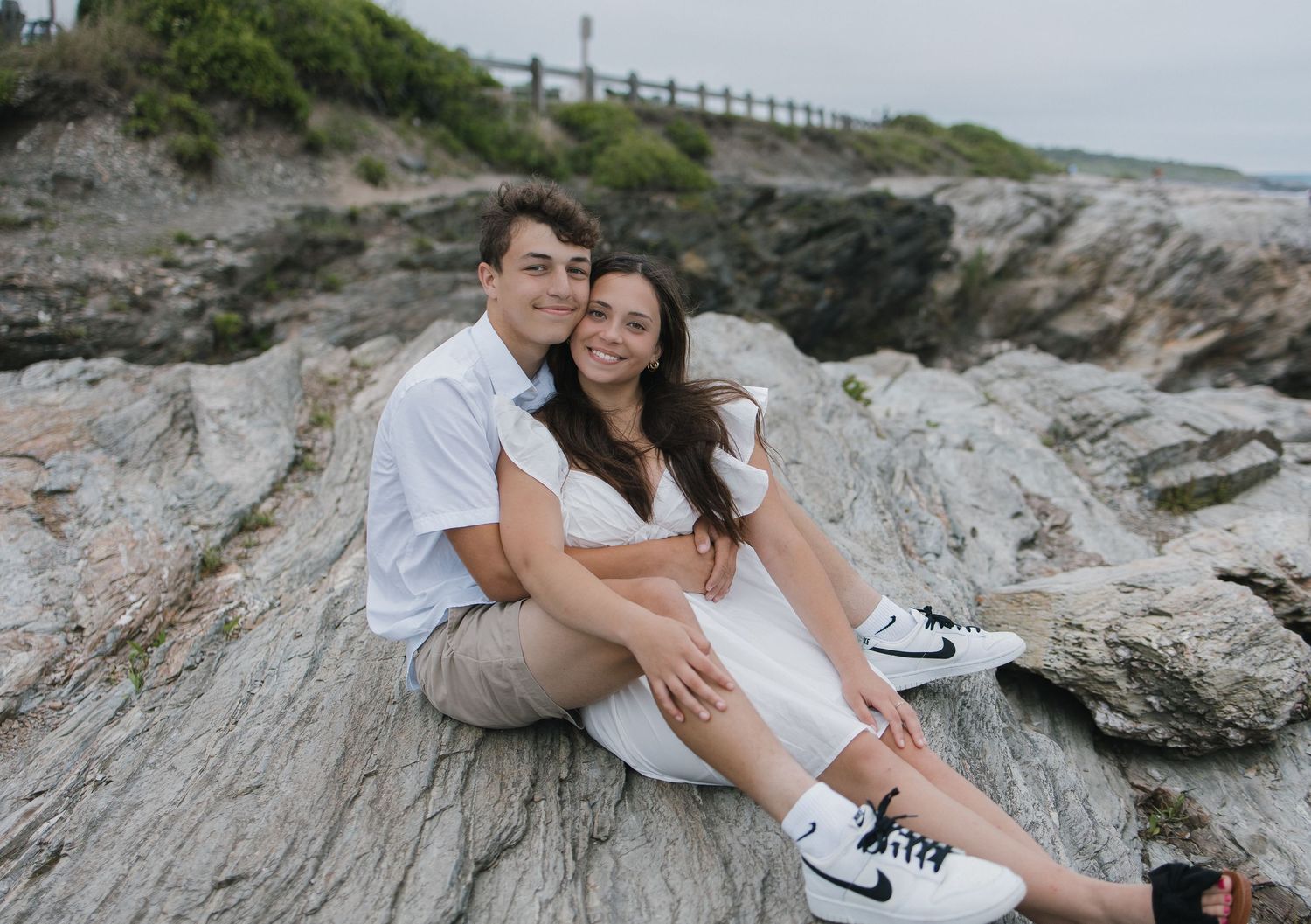 A couple shares an intimate moment while sitting on coastal rocks near the ocean.