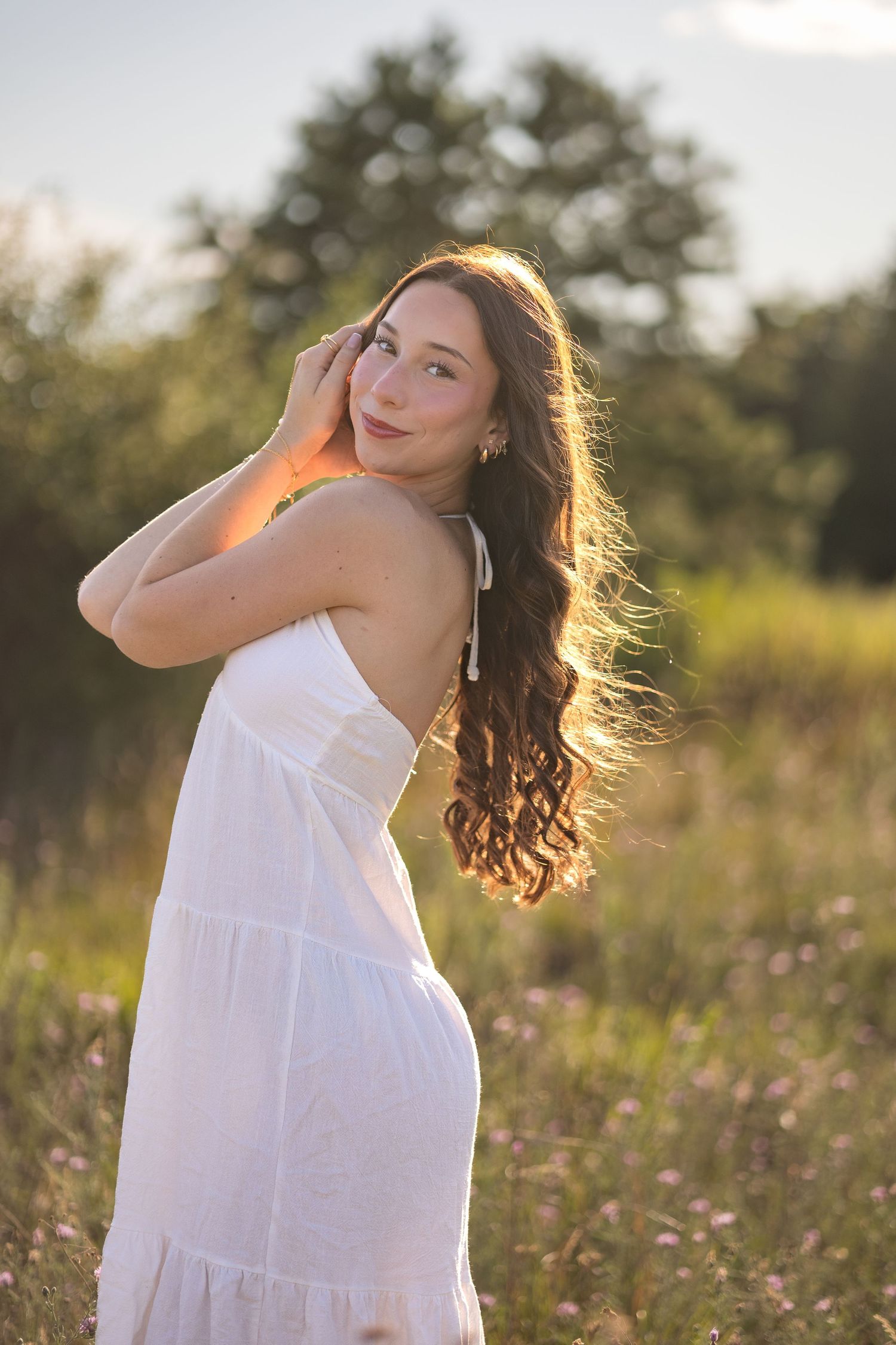 Woman in white sundress twirls gracefully in a sunlit wildflower meadow during golden hour.