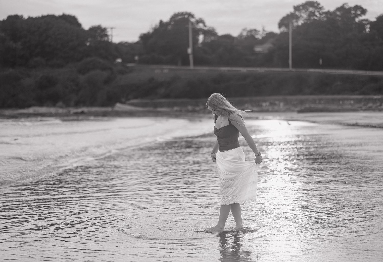 A silhouetted figure walks along a misty beach shoreline at sunset with water reflections.