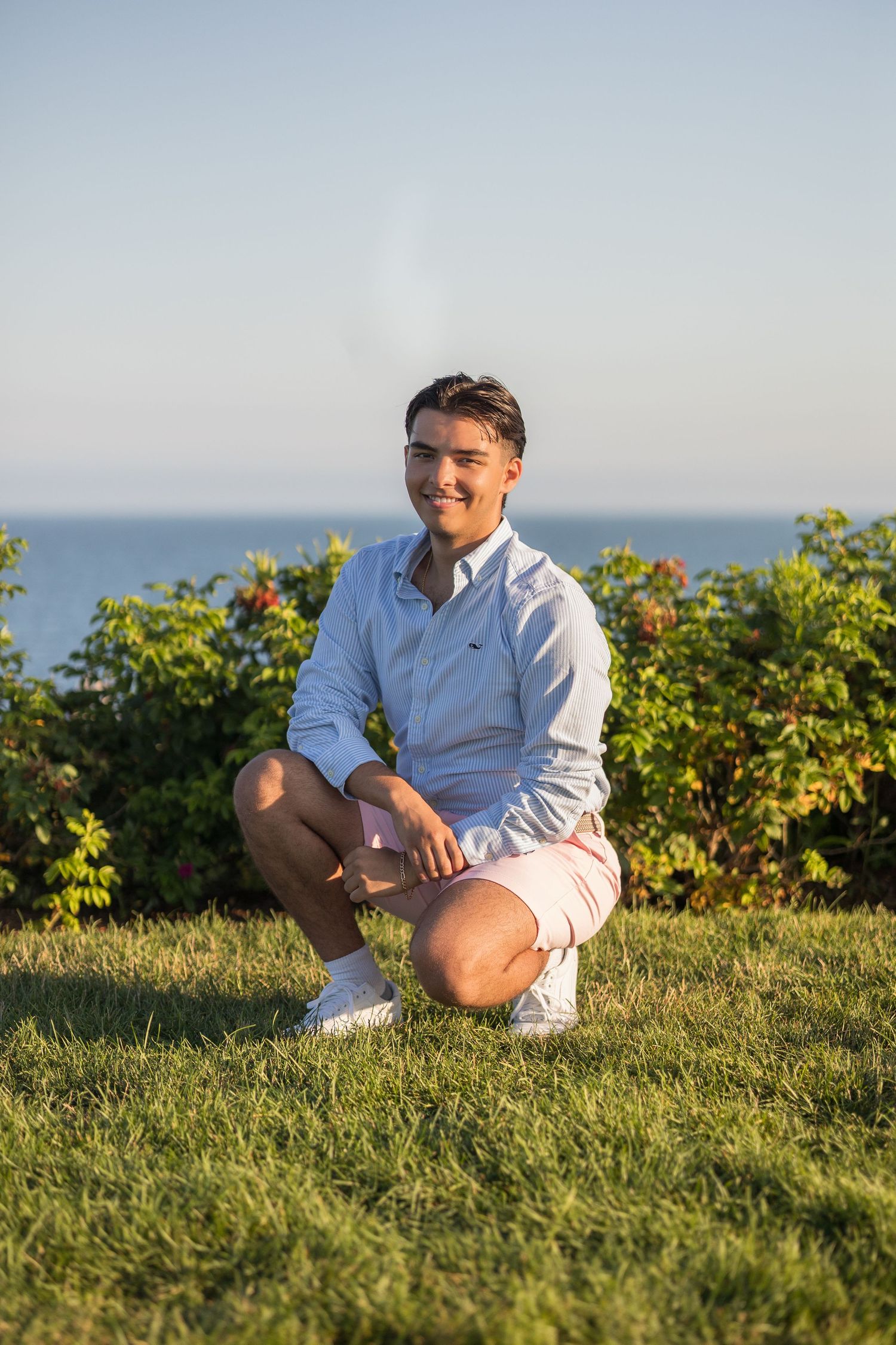 Person relaxing on a grassy hillside overlooking the ocean during golden hour.