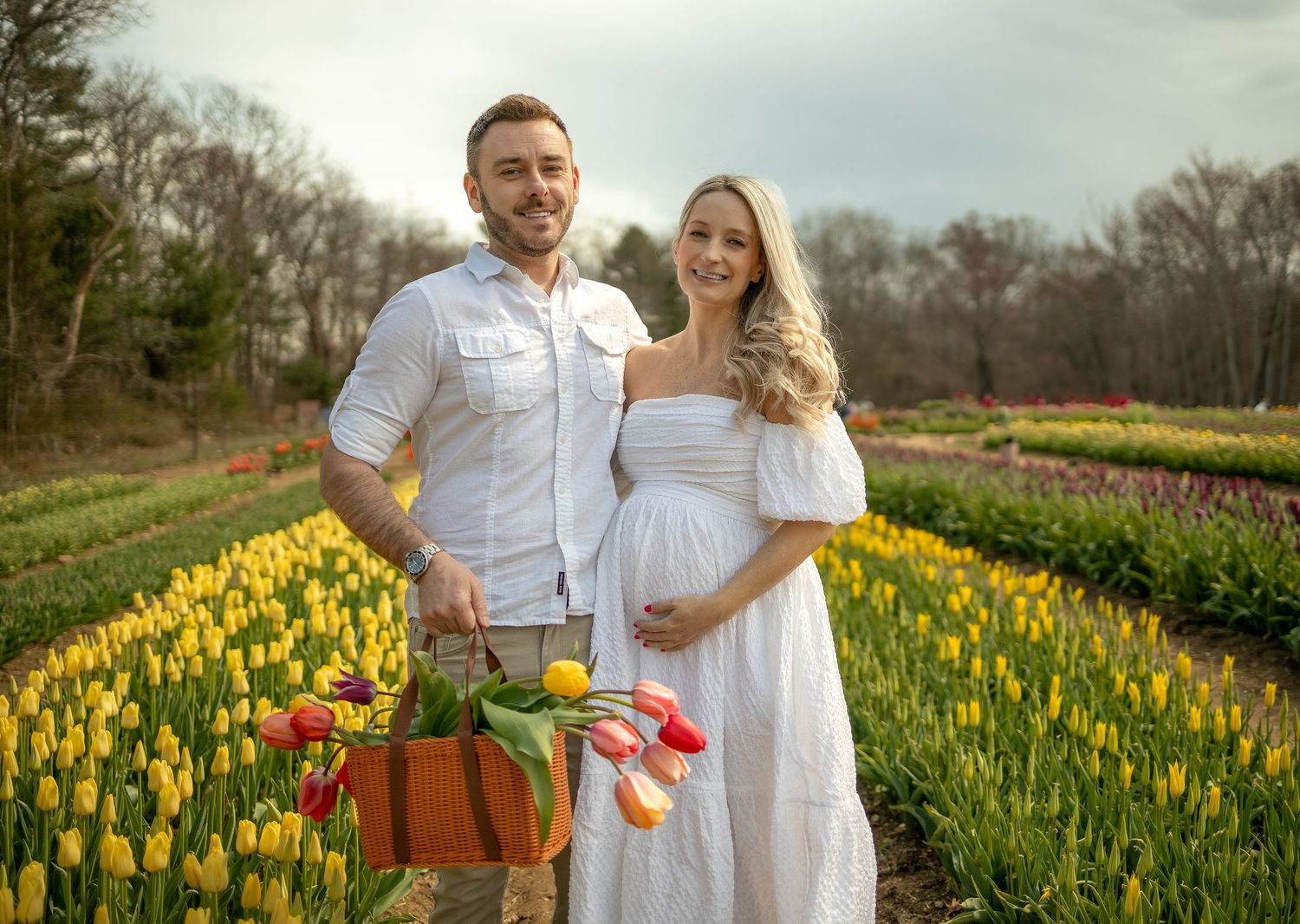A romantic couple posing in a field of bright yellow tulips with a rustic basket.