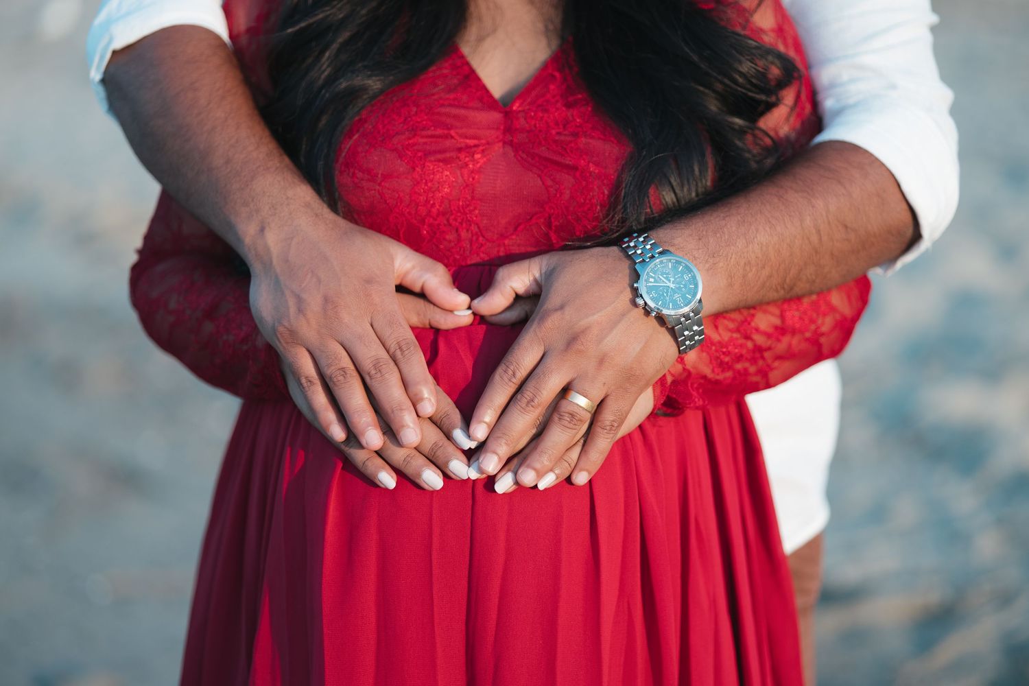 Intimate close-up of hands forming a heart shape over a red maternity dress.