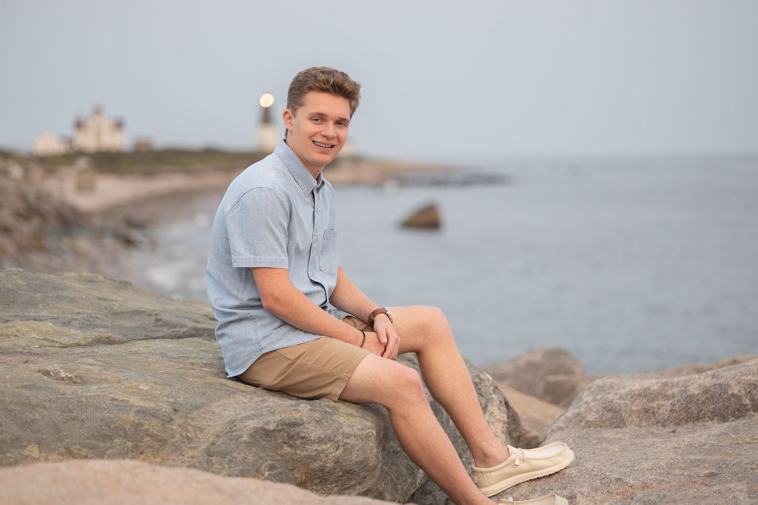 A relaxed pose on coastal rocks with ocean and cloudy sky in the background.