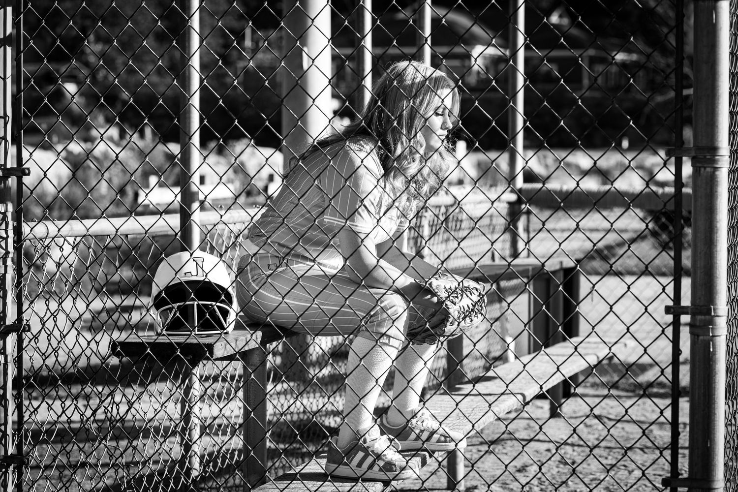 A black and white photo shows a person playing tennis on an outdoor court with chain link fencing visible.