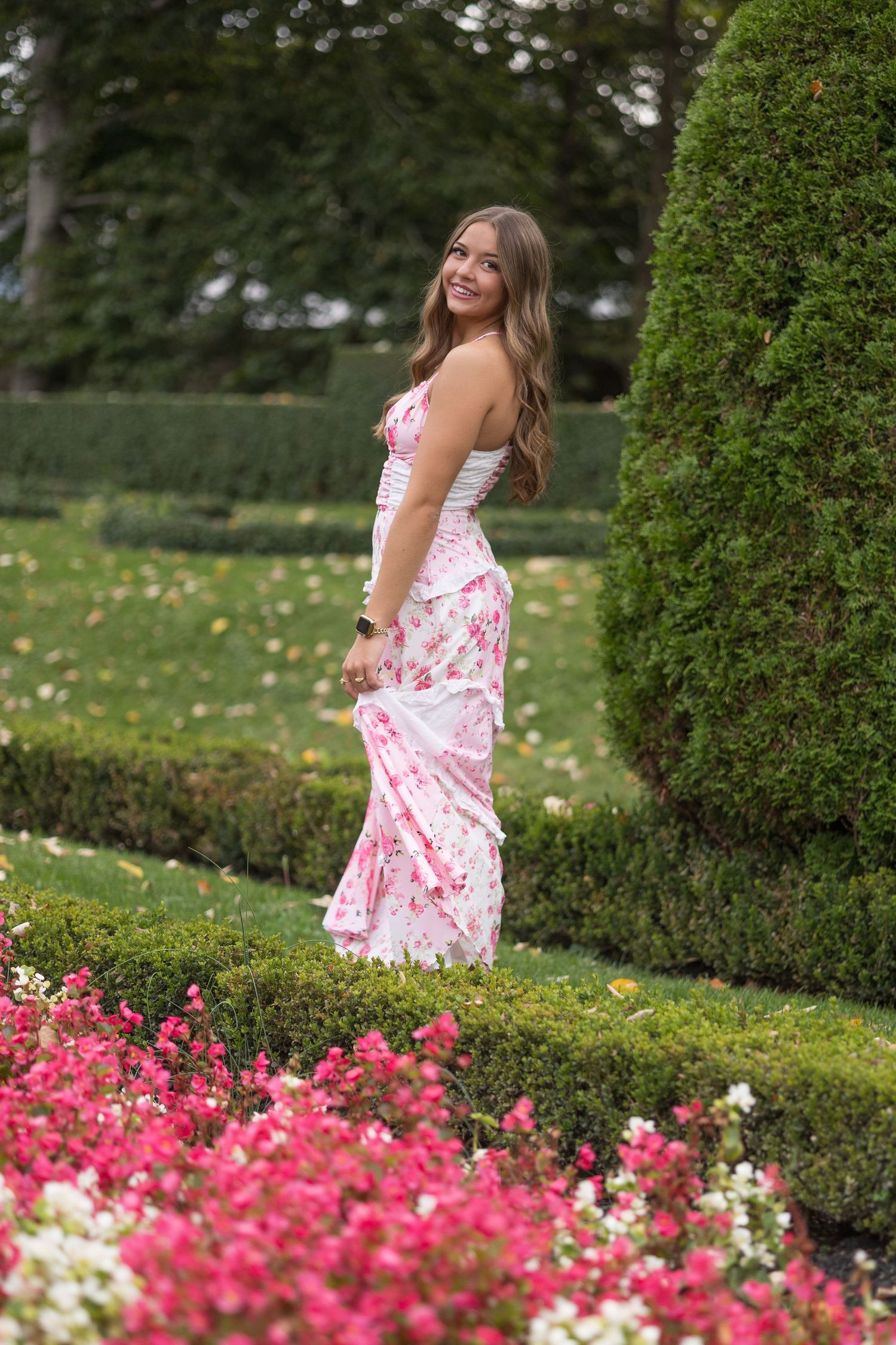 Pink floral dress photographed in a garden setting with blooming roses and manicured hedges.