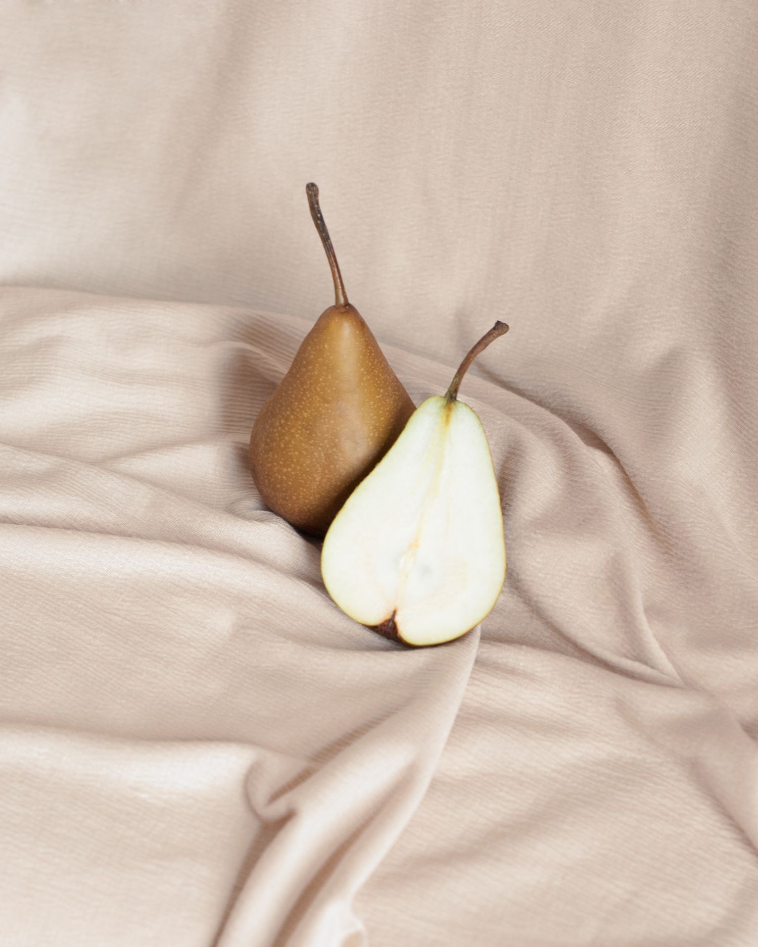 Artfully composed pears on cream colored fabric with soft natural lighting.