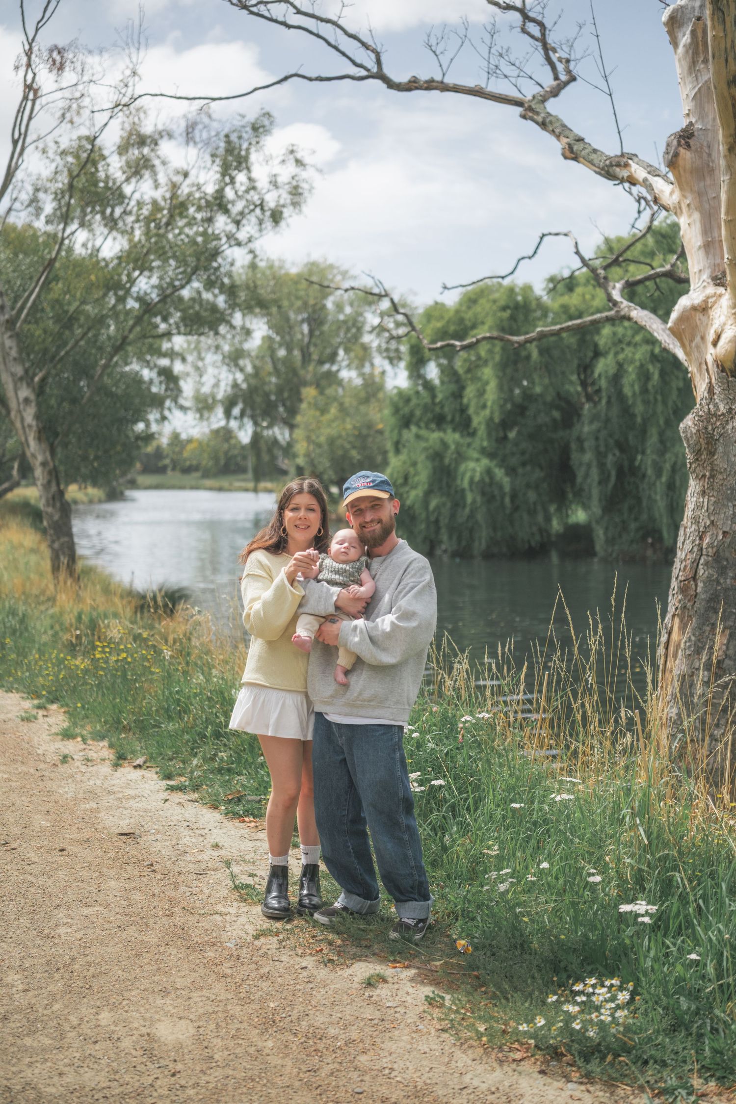 A dirt path winds along a scenic lake with wildflowers and willow trees creating a peaceful natural setting.