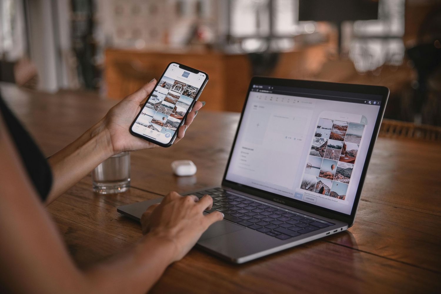 Person holding smartphone displaying photo gallery app beside open laptop showing image editing website on wooden desk.