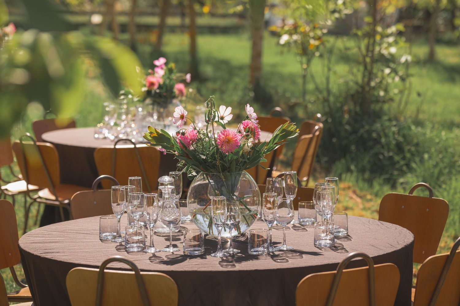 Elegant outdoor round table set with glass stemware and pink floral centerpiece for a garden wedding reception.