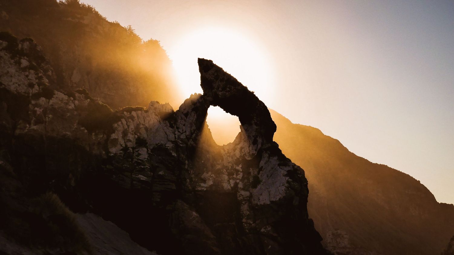 A stunning panoramic view of mountain peaks silhouetted against a golden sunset with dramatic clouds in the sky.