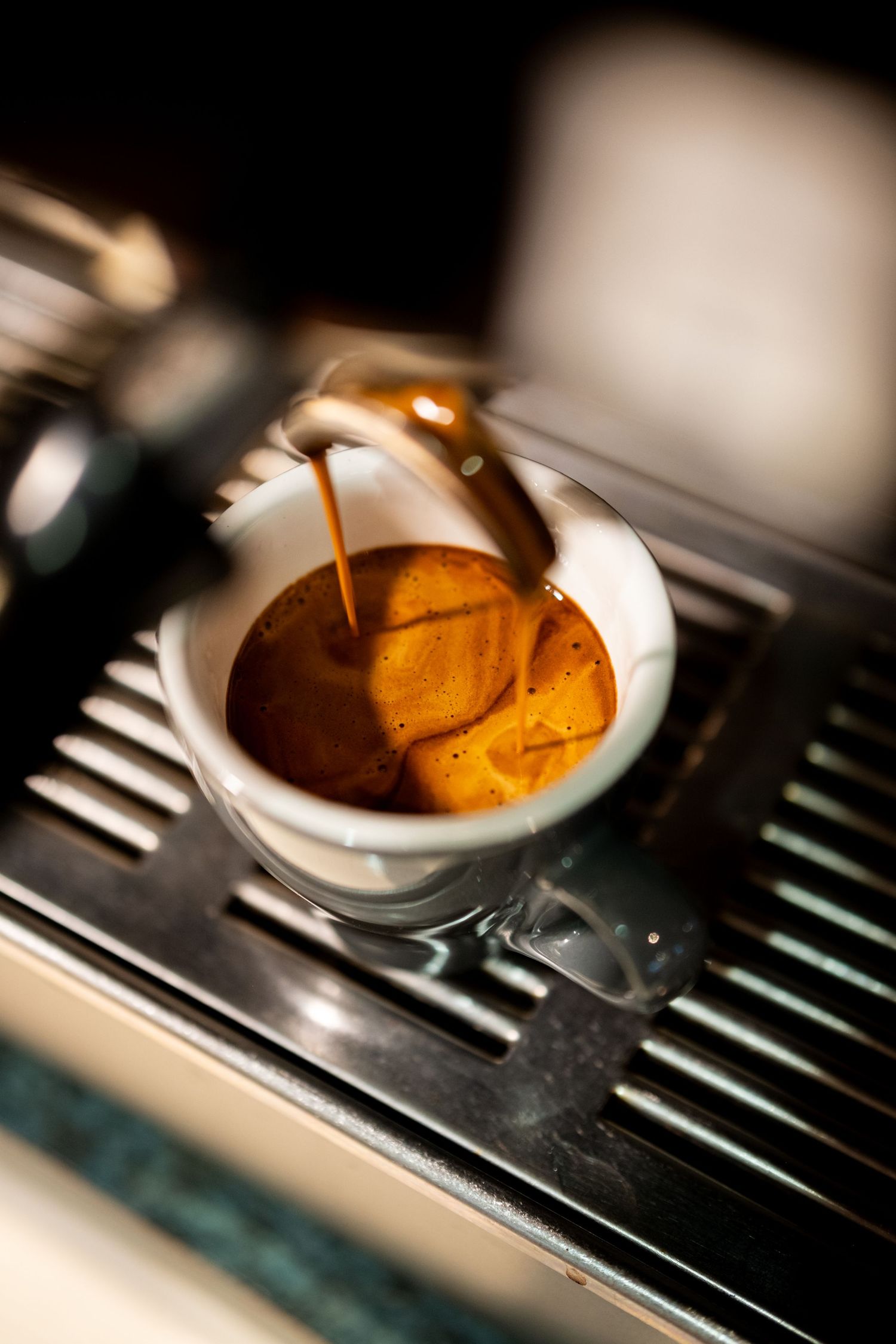 Espresso machine brewing rich, golden crema into a small glass cup on a stainless steel drip tray.