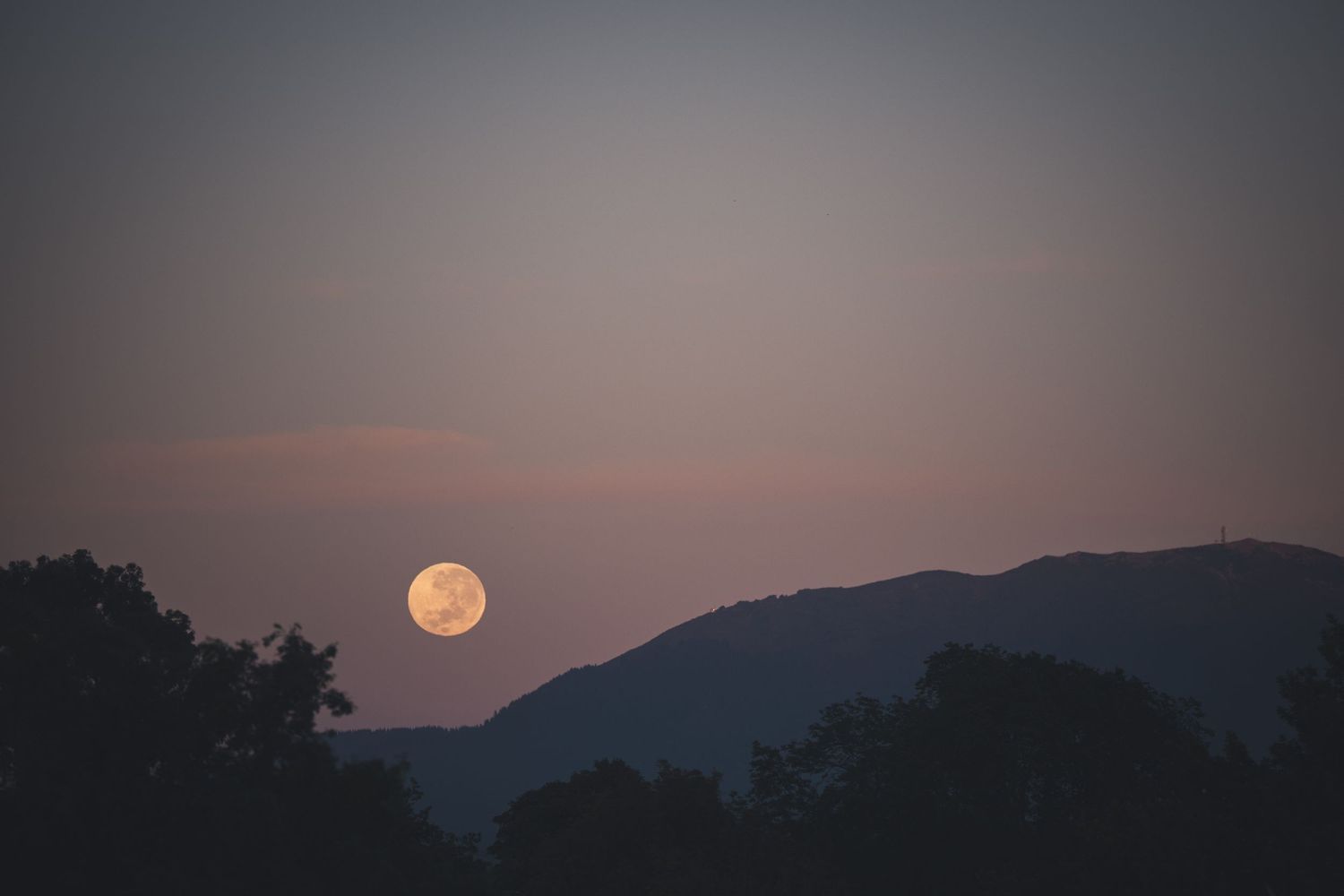 A stunning full moon rises over silhouetted mountain peaks during a dusky purple sunset.