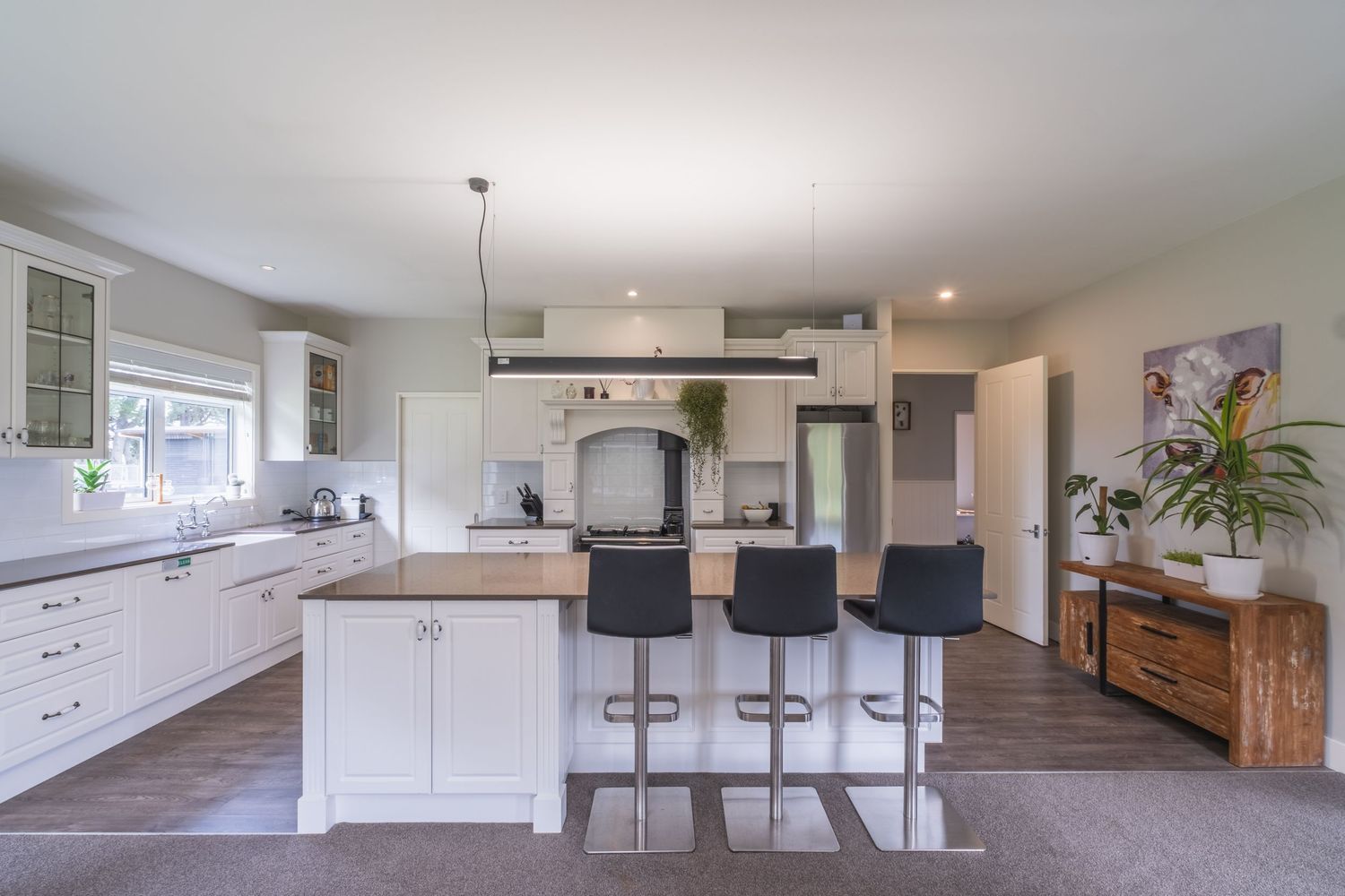 Modern white kitchen with island bar seating, pendant lighting, and dark hardwood floors in an open-plan layout.