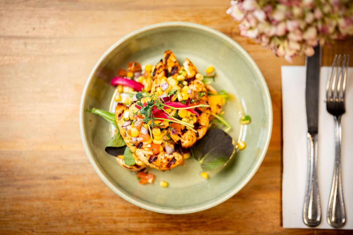Gourmet roasted cauliflower dish served in a green ceramic bowl on a wooden table with cutlery.