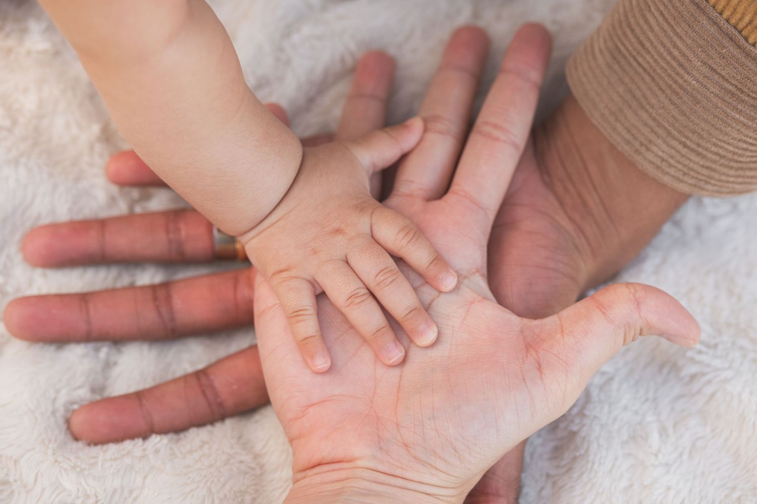 A tiny baby hand rests gently on top of an adult's open palm against a soft white background.
