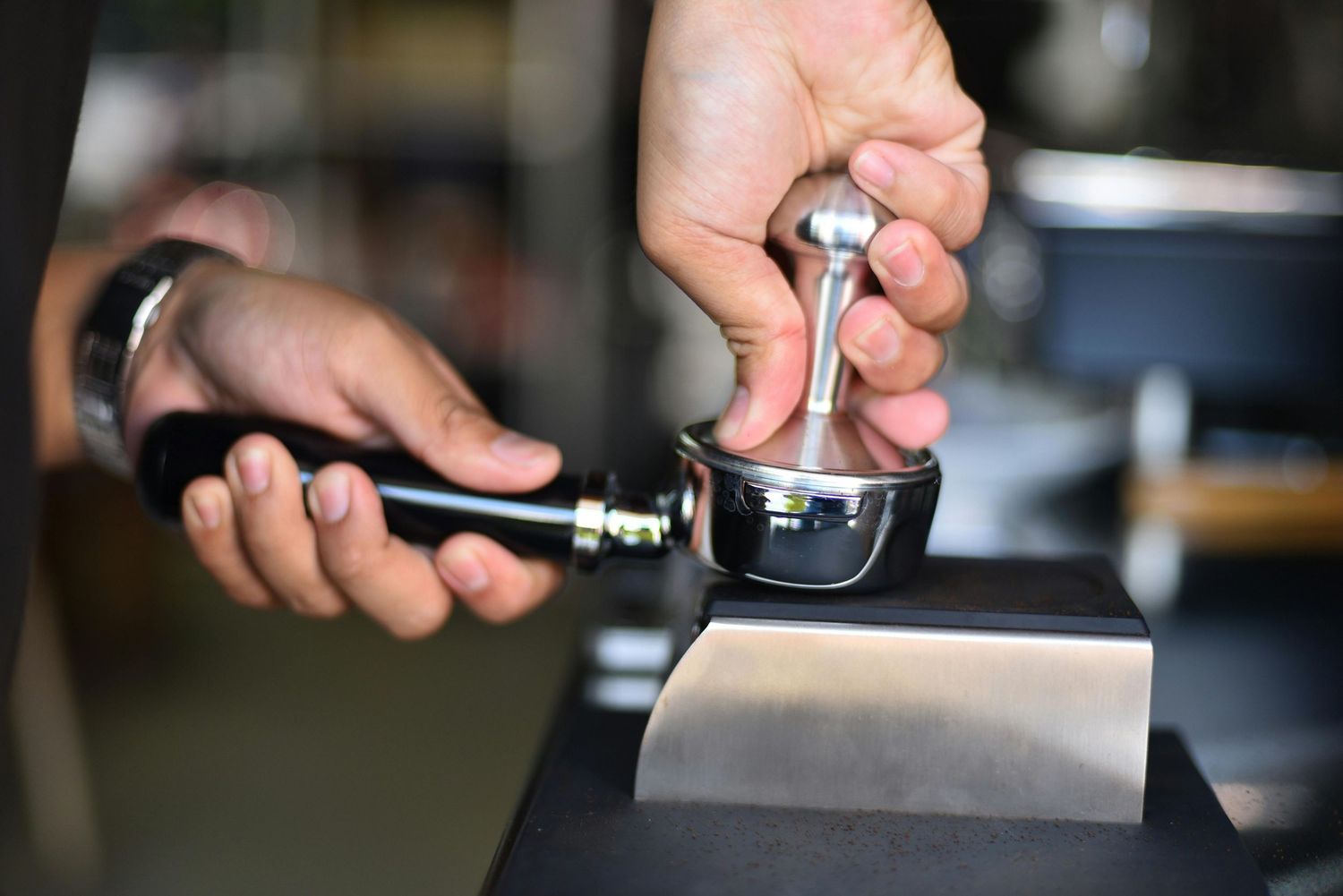 Barista tamping fresh espresso grounds into a portafilter on a knock box for coffee preparation.