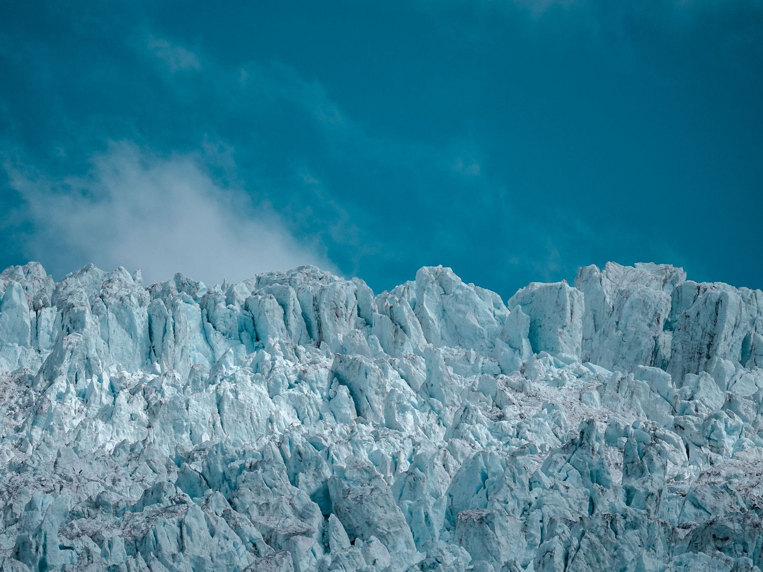 Panoramic view of a majestic glacier with jagged ice formations against a deep turquoise sky.