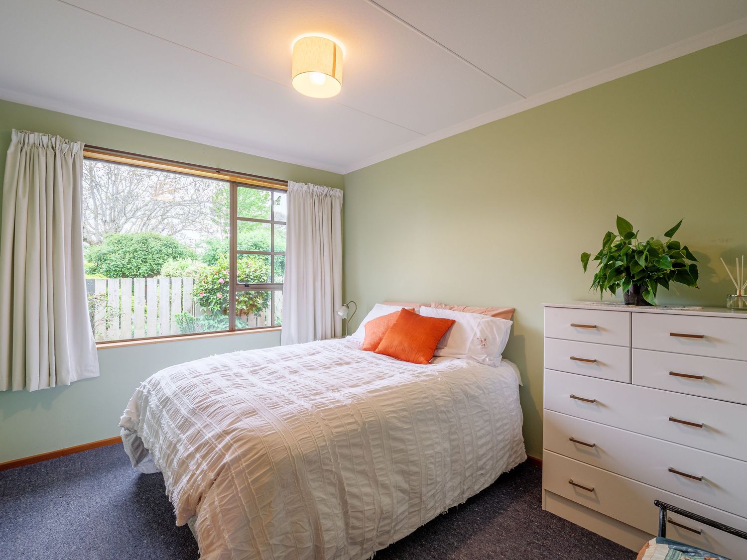 Bright bedroom with white furniture, green walls, orange accents, and natural light streaming through windows.