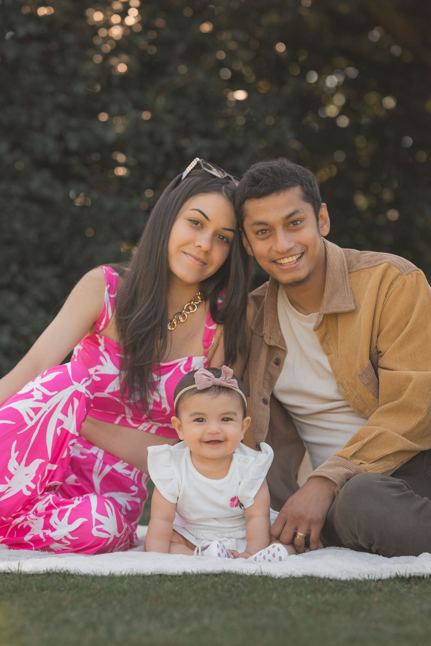 Family sitting together on white blanket outdoors with bokeh lights in background.