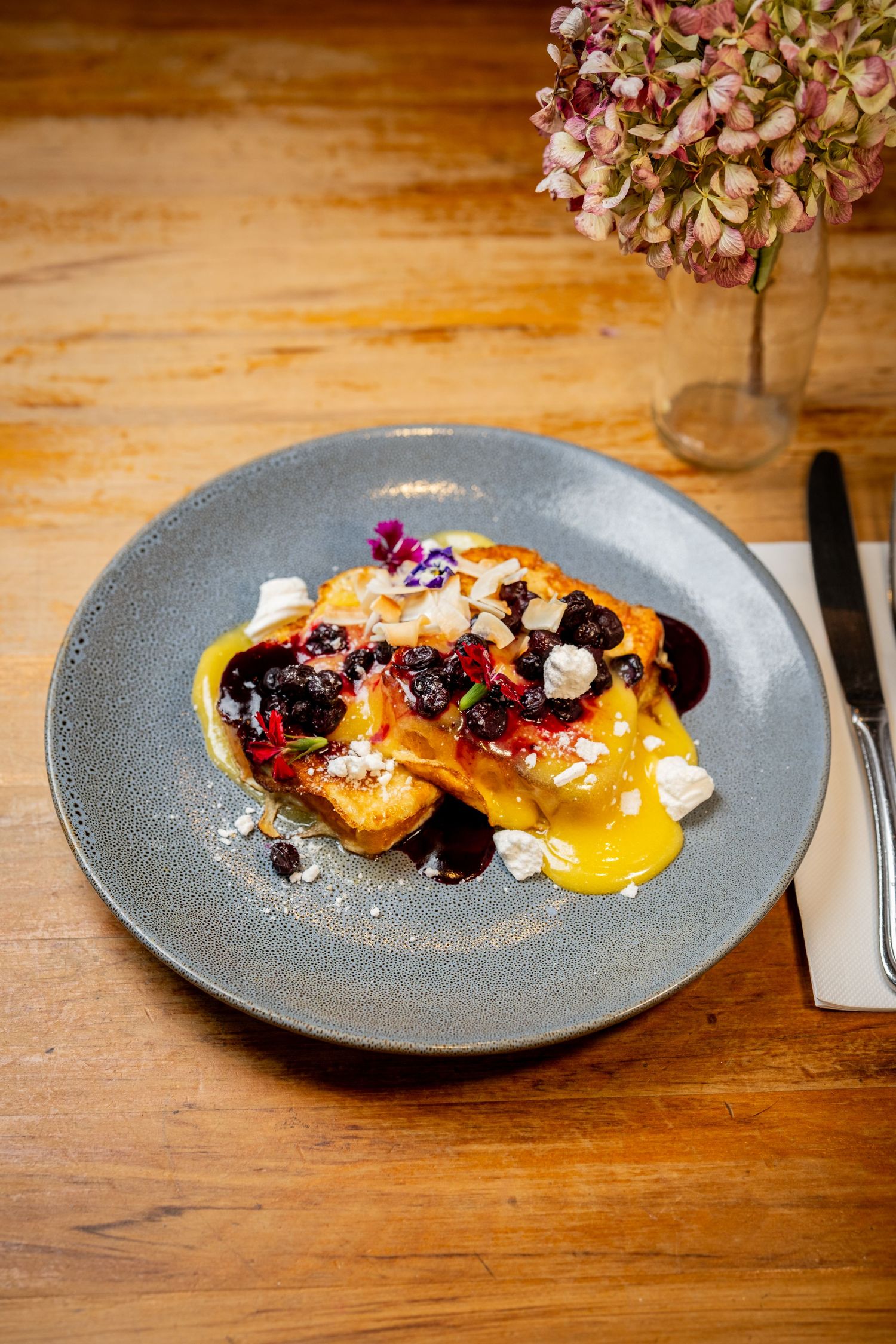 Elegant French toast with blueberry compote, mango coulis, and cream cheese on a gray ceramic plate.