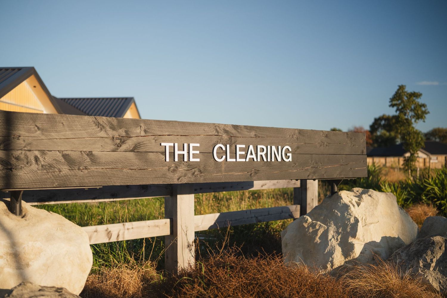 Wooden sign reading The Clearing mounted on posts with rocks and dry grass in a scenic outdoor setting.