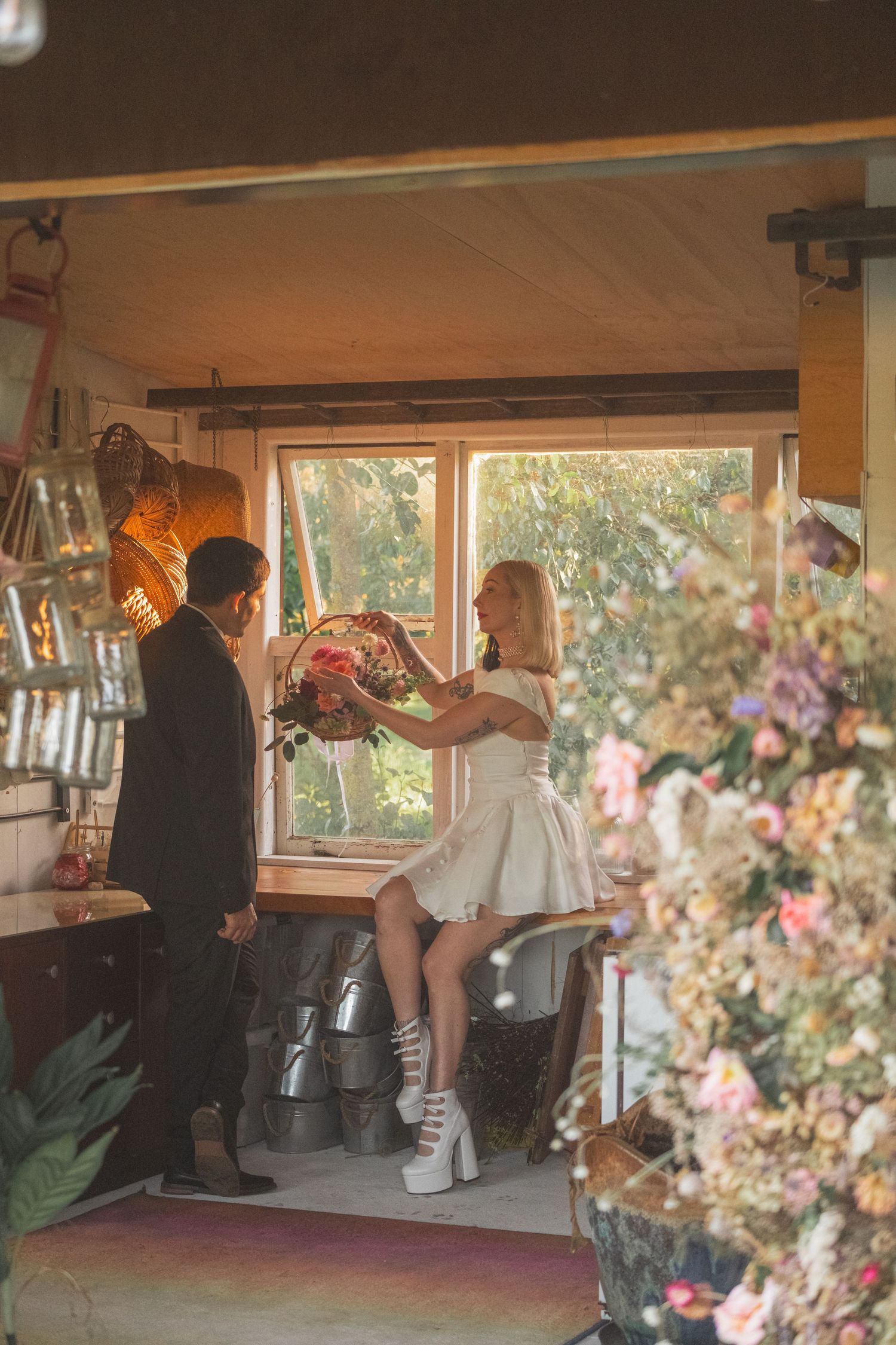 Couple exchanging flowers in a cozy, warmly lit room with floral decor and a large window.