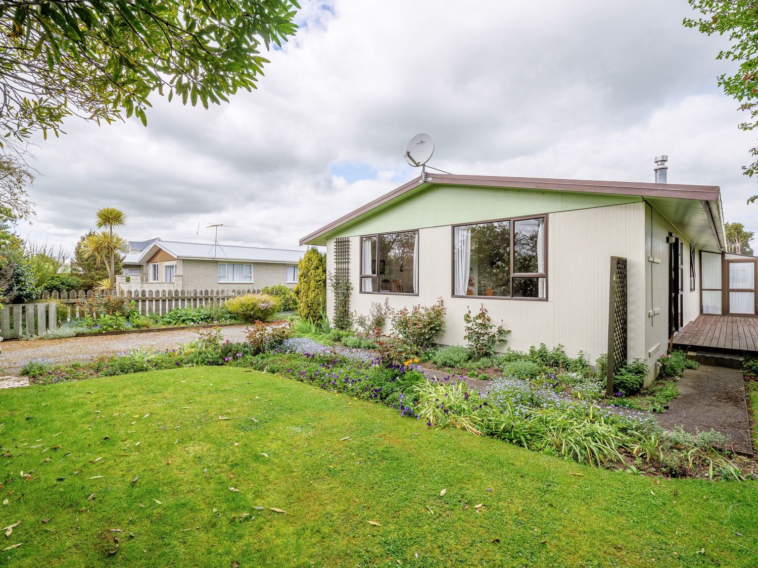 Panoramic view of a white mobile home with green lawn and landscaping against cloudy sky.